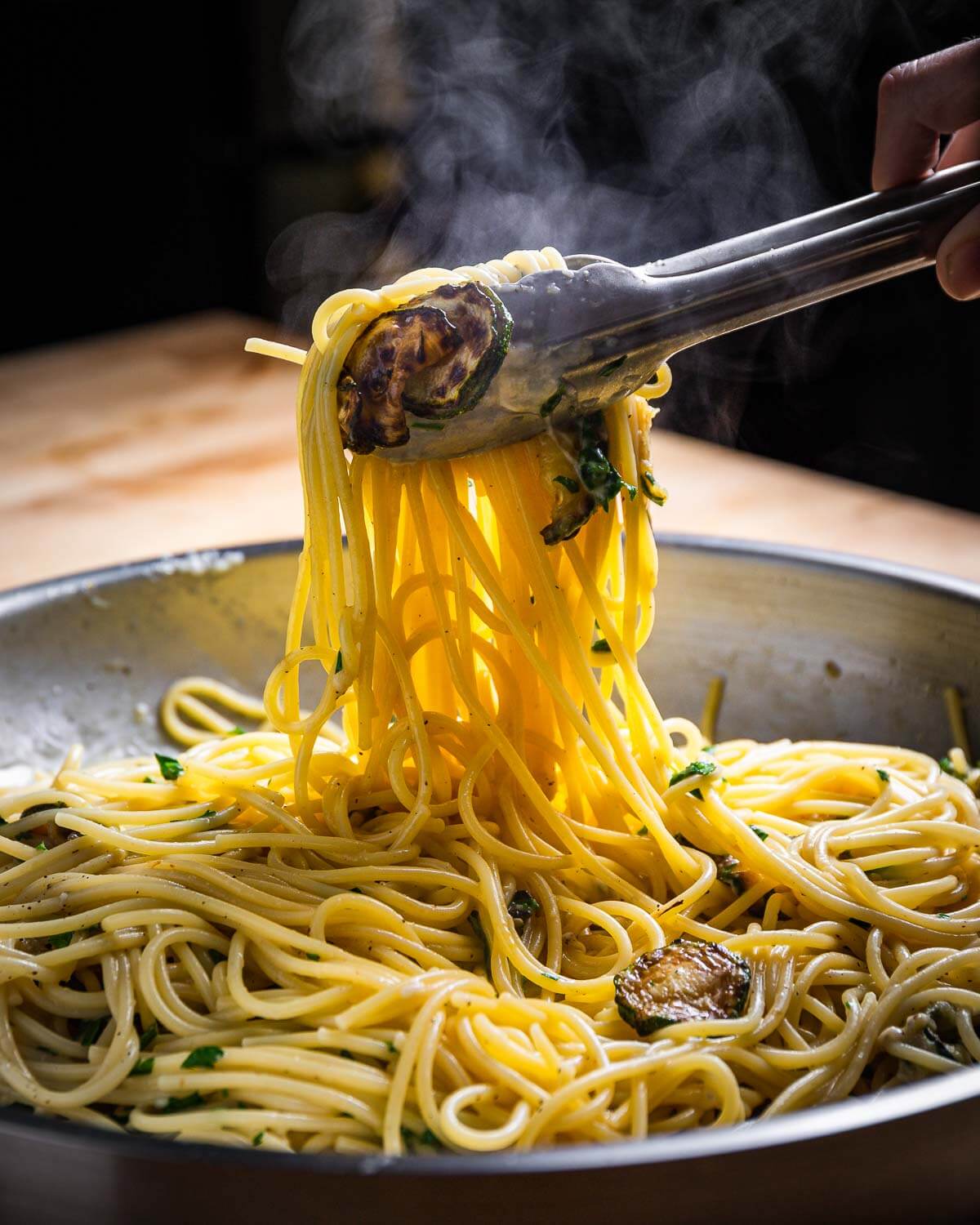 Spaghetti being pulled out of pan and held in tongs.