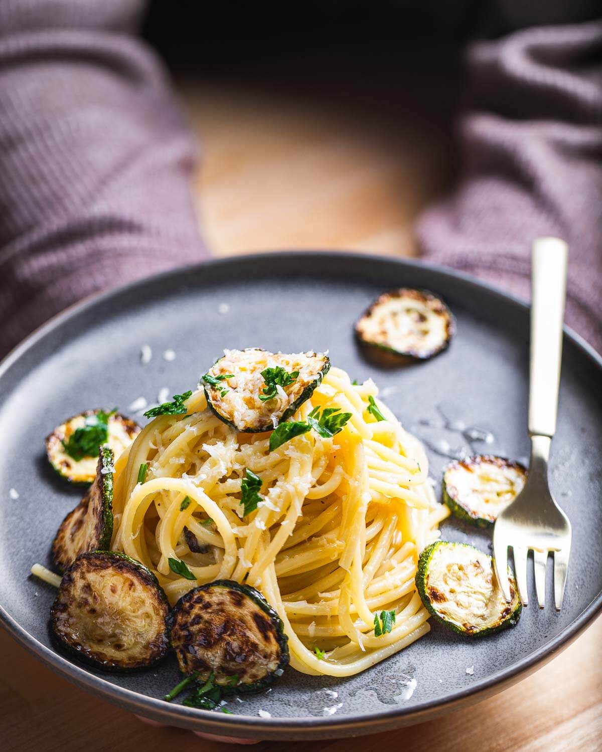 Grey plate held in hands with a nest of spaghetti and seared zucchini.