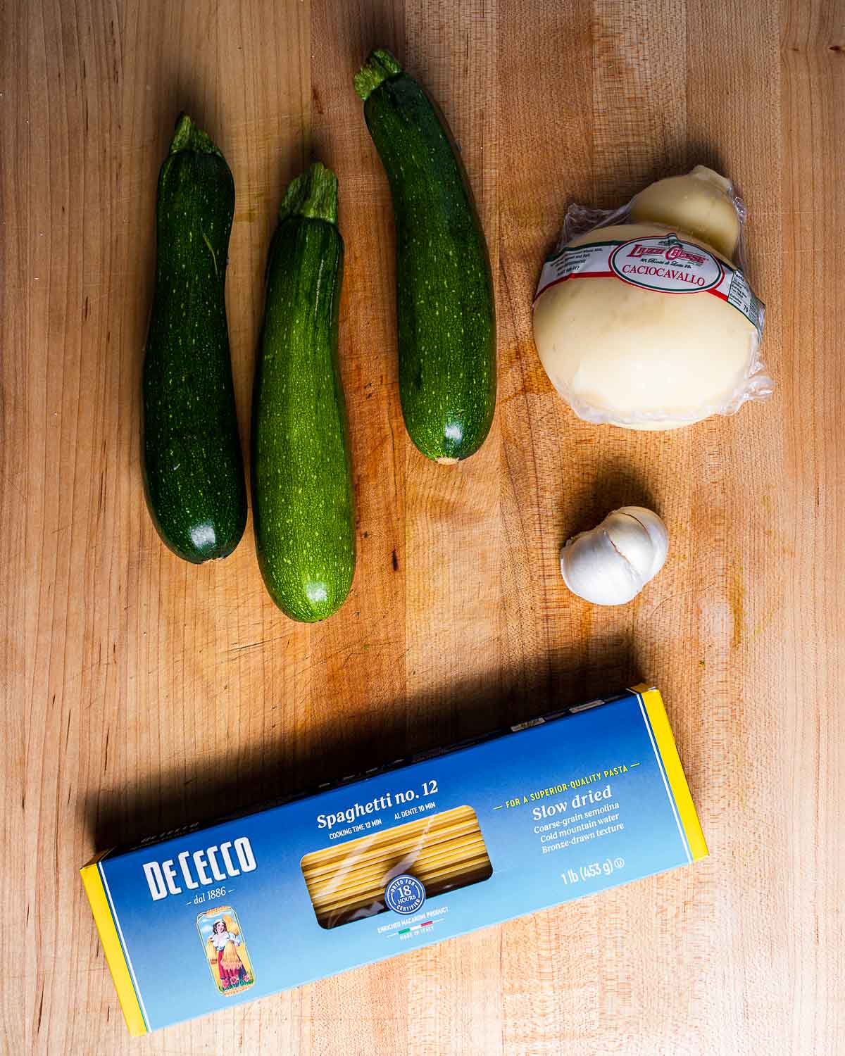 Ingredients shown: 3 medium zucchini, caciocavallo cheese, box of spaghetti, and head of garlic.
