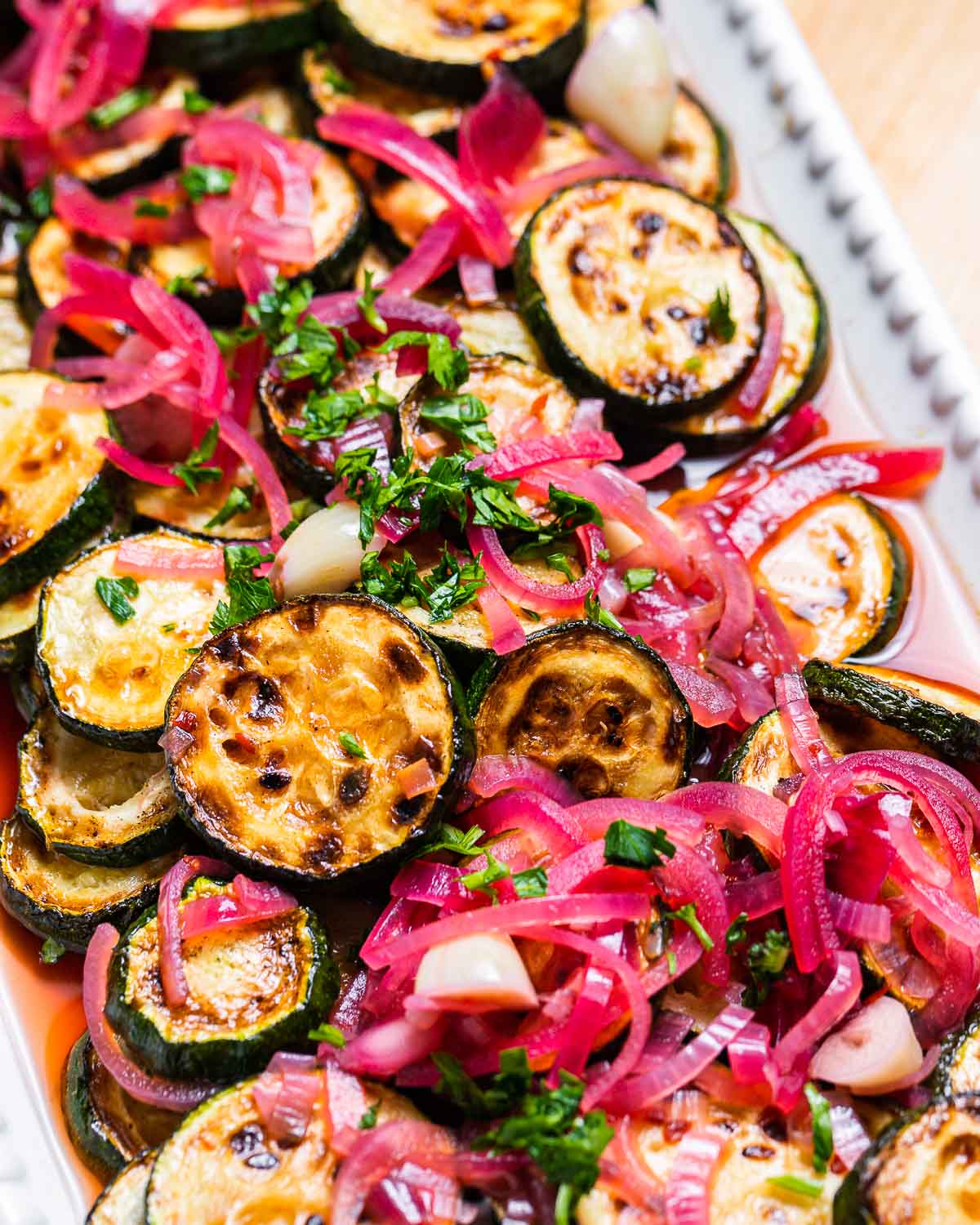 Sweet and sour zucchini with red onions in white platter.