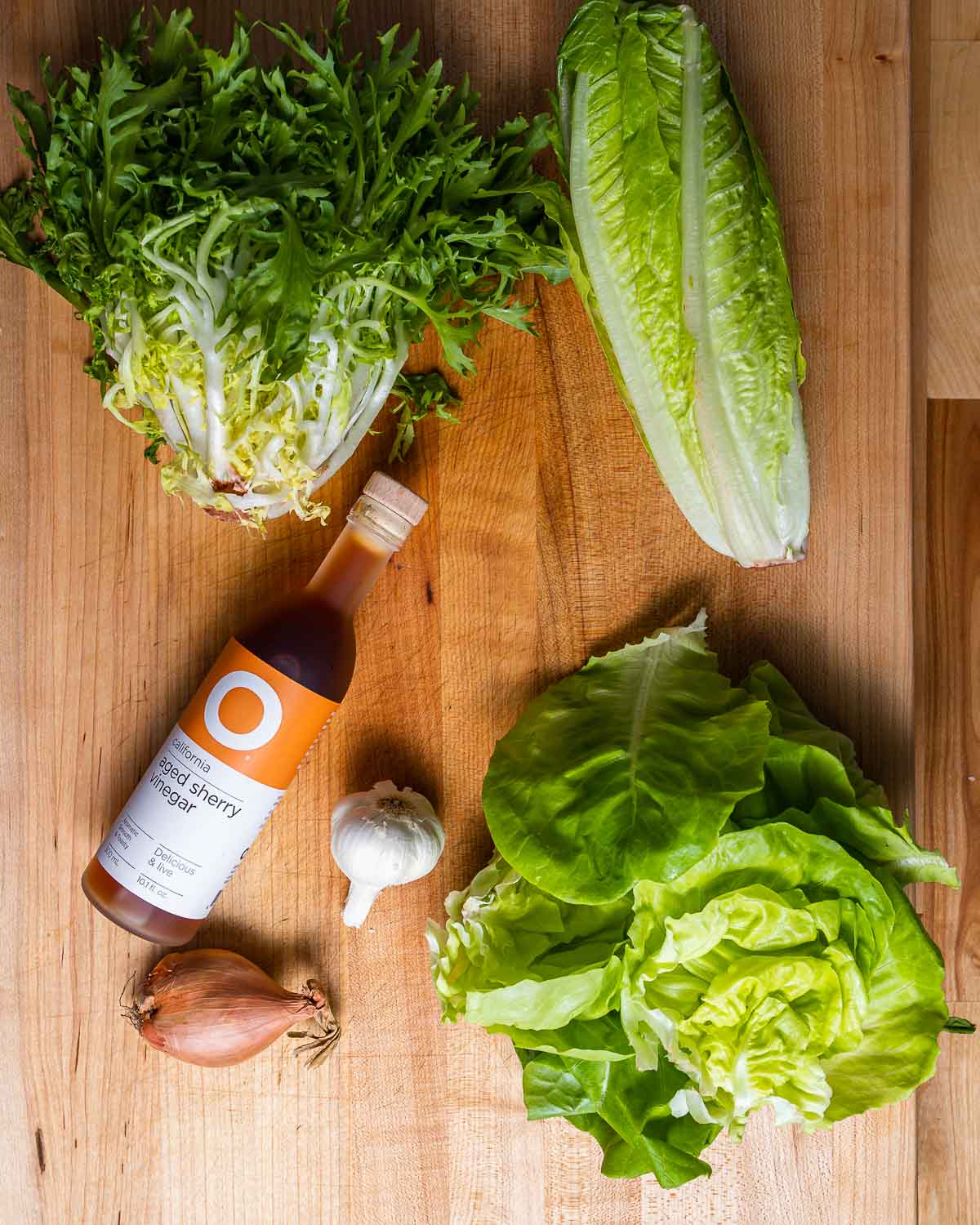Ingredients shown: frisee, romaine, and Boston lettuce along with bottle of sherry vinegar, head of garlic, and shallot.
