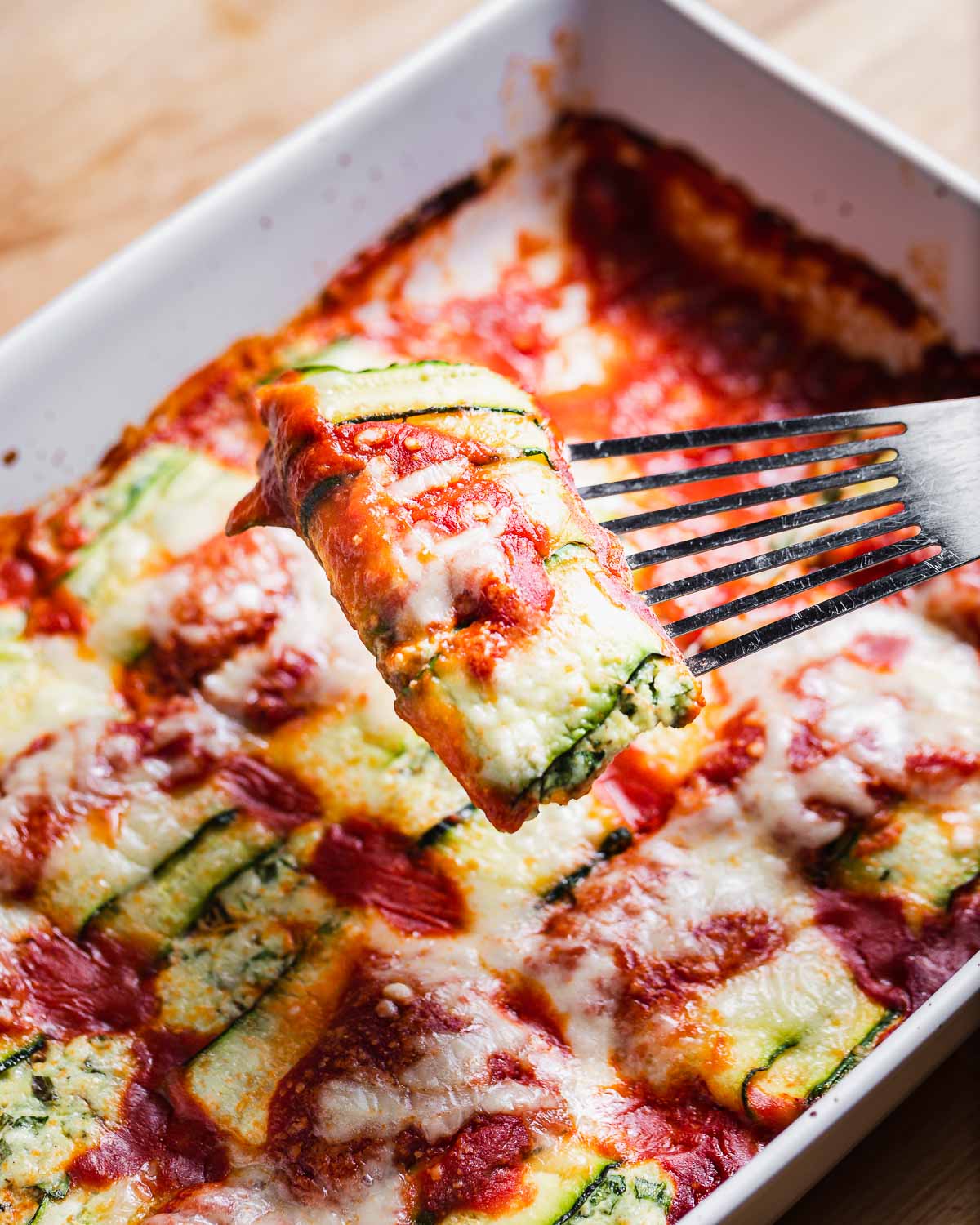 One piece of zucchini roll ups held with fish spatula over baking dish.