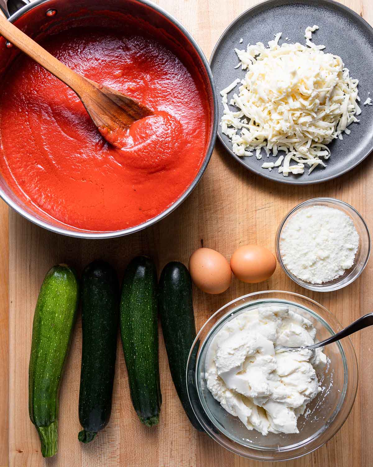 Ingredients shown: pot of marinara, mozzarella cheese, 4 zucchini, 2 eggs, Pecorino Romano and ricotta cheese.