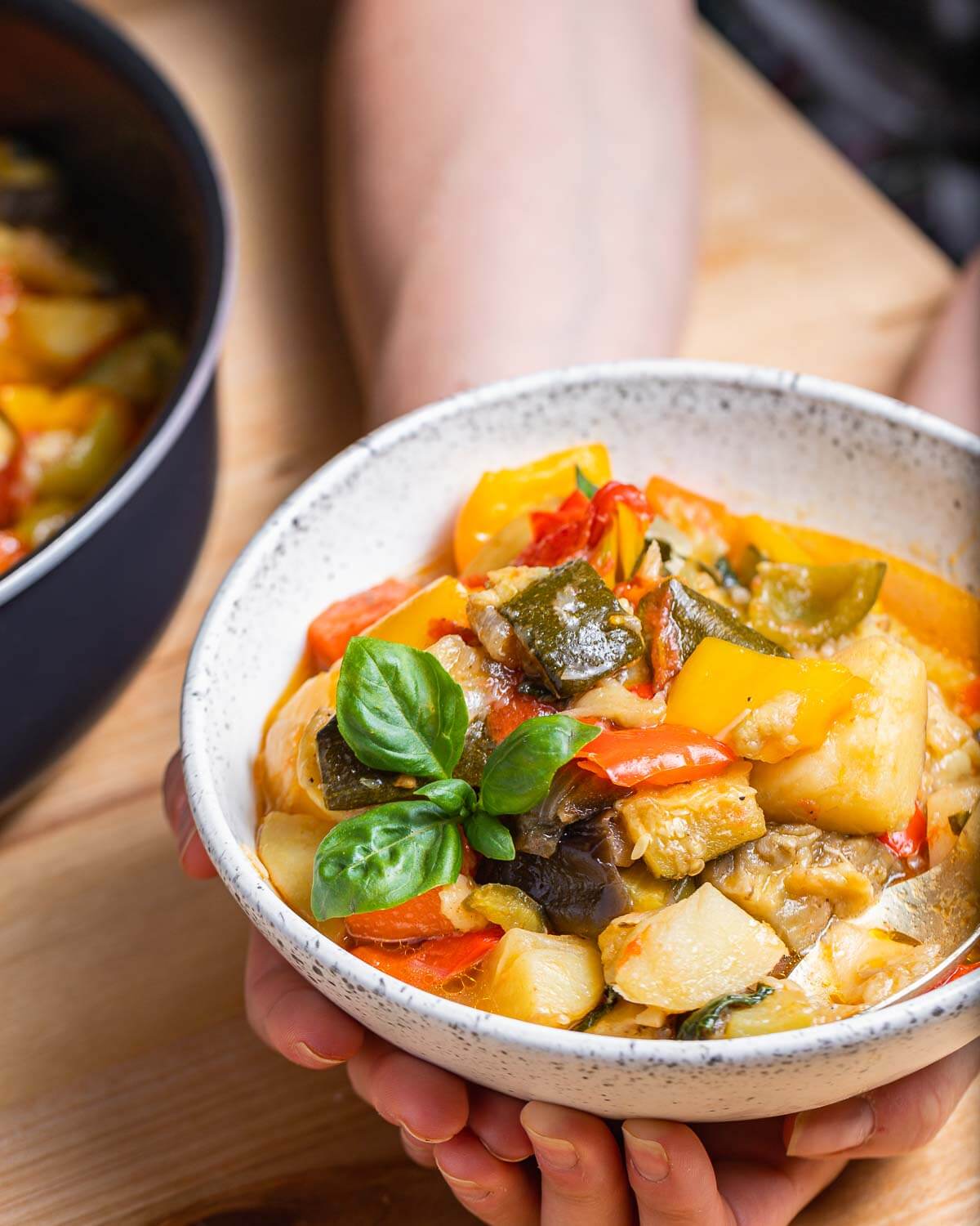 Italian vegetable stew in white bowl held in hands.