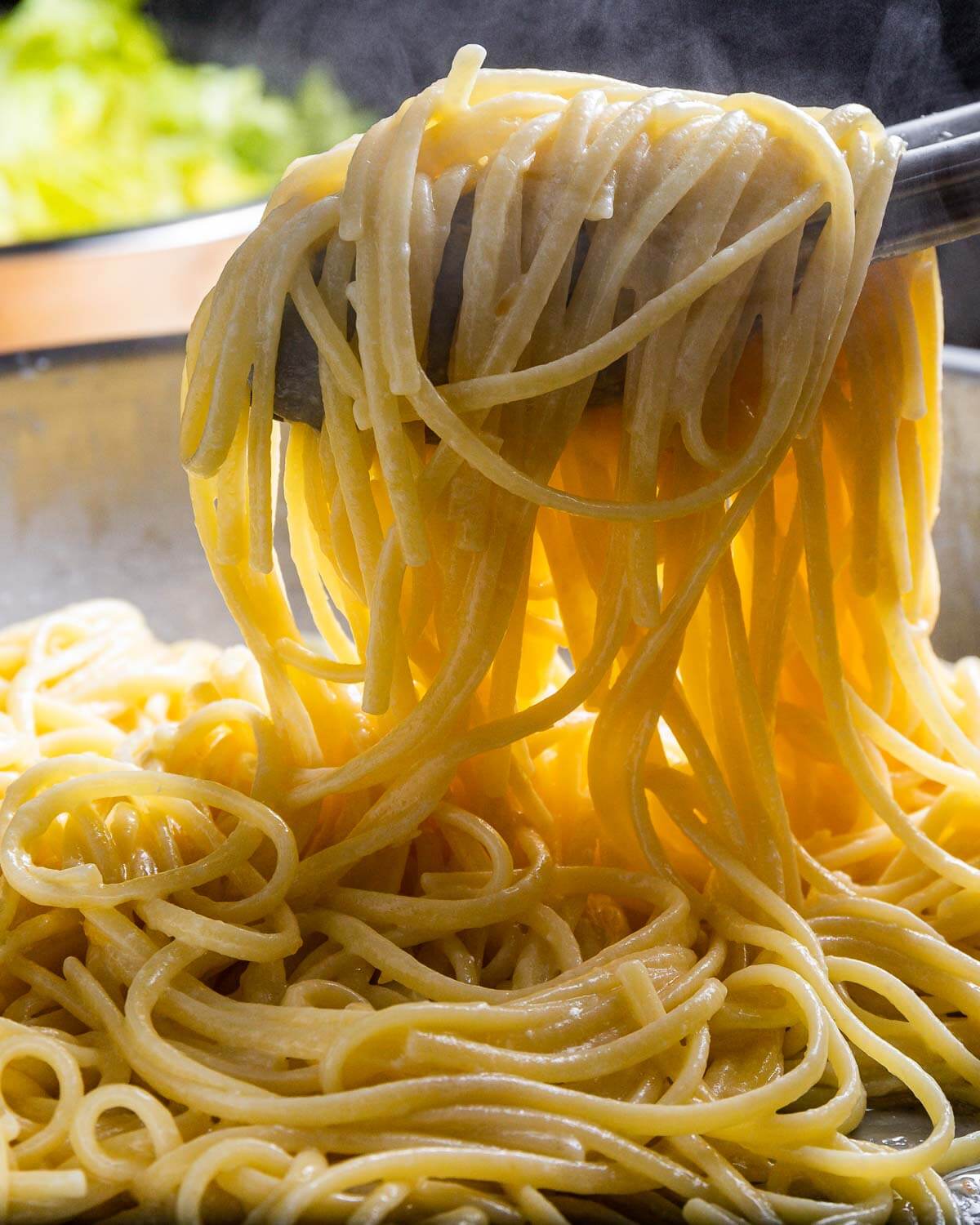 Tongs holding linguine with cheese.