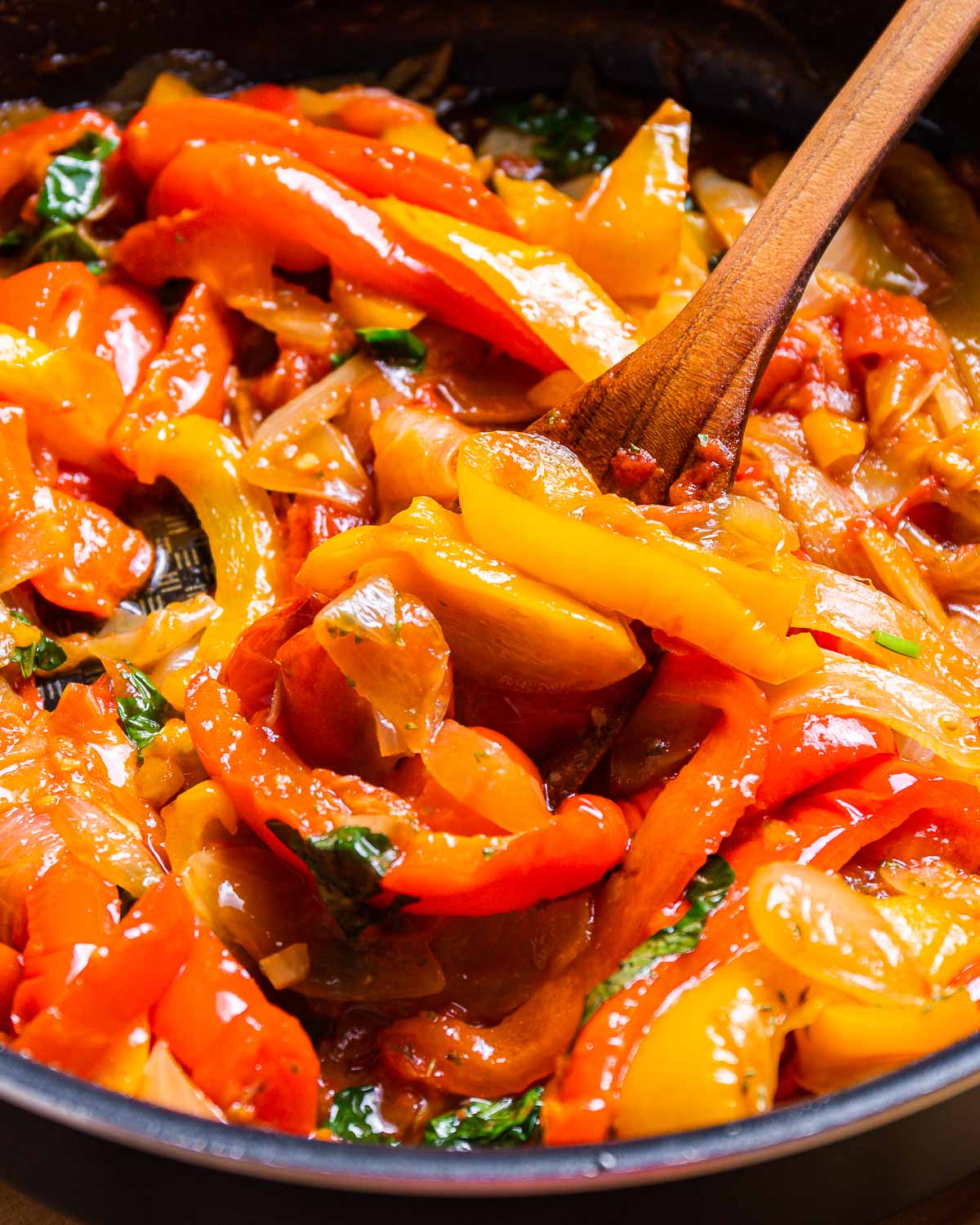 Peppers and onions in black pan with wooden spoon.