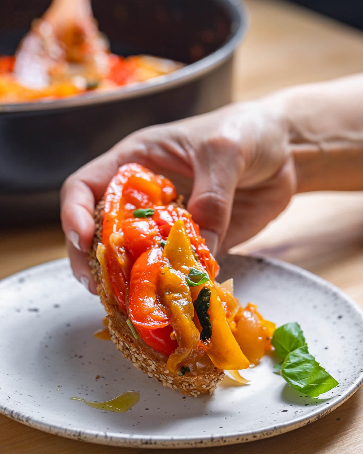 Toaste with peperonata held in hands over white plate.