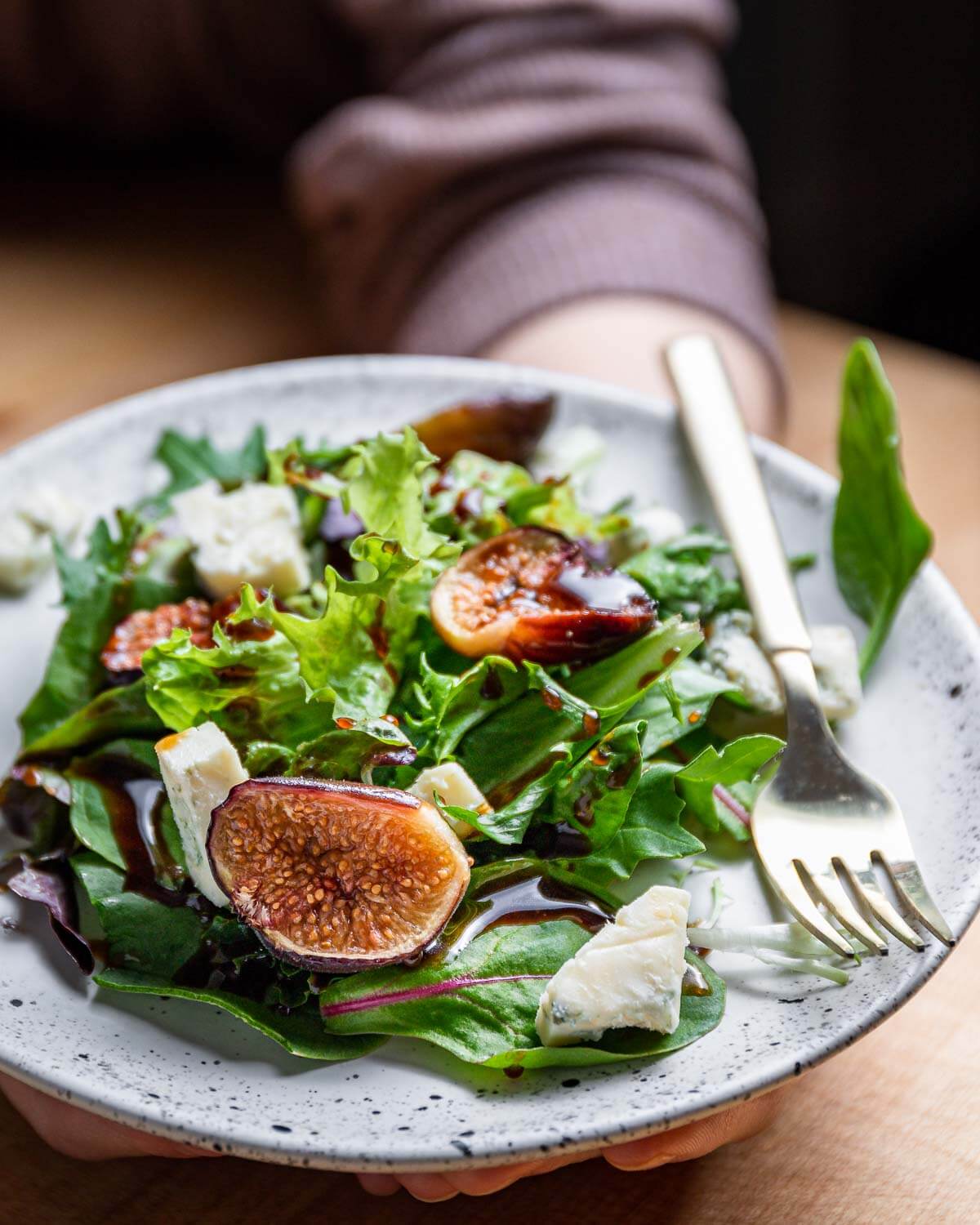 White plate with salad greens, gorgonzola cheese, and figs being held in hands.