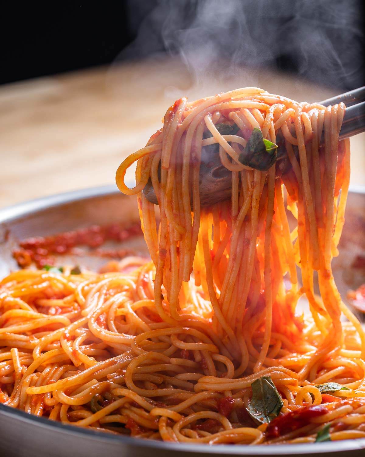 Tongs pulling out hot spaghetti arrabbiata with steam showing.