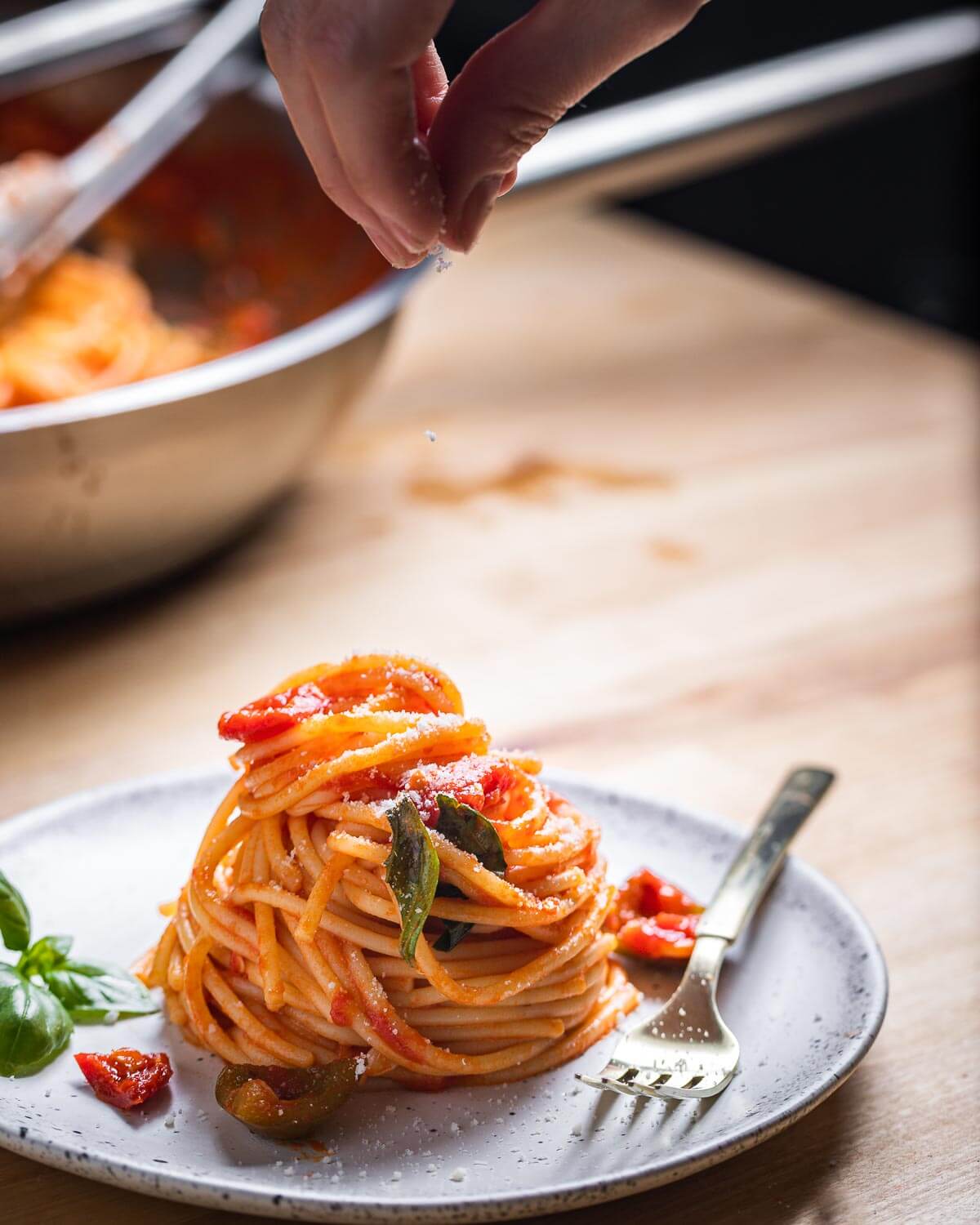 Sprinkling cheese onto plate of spaghetti.