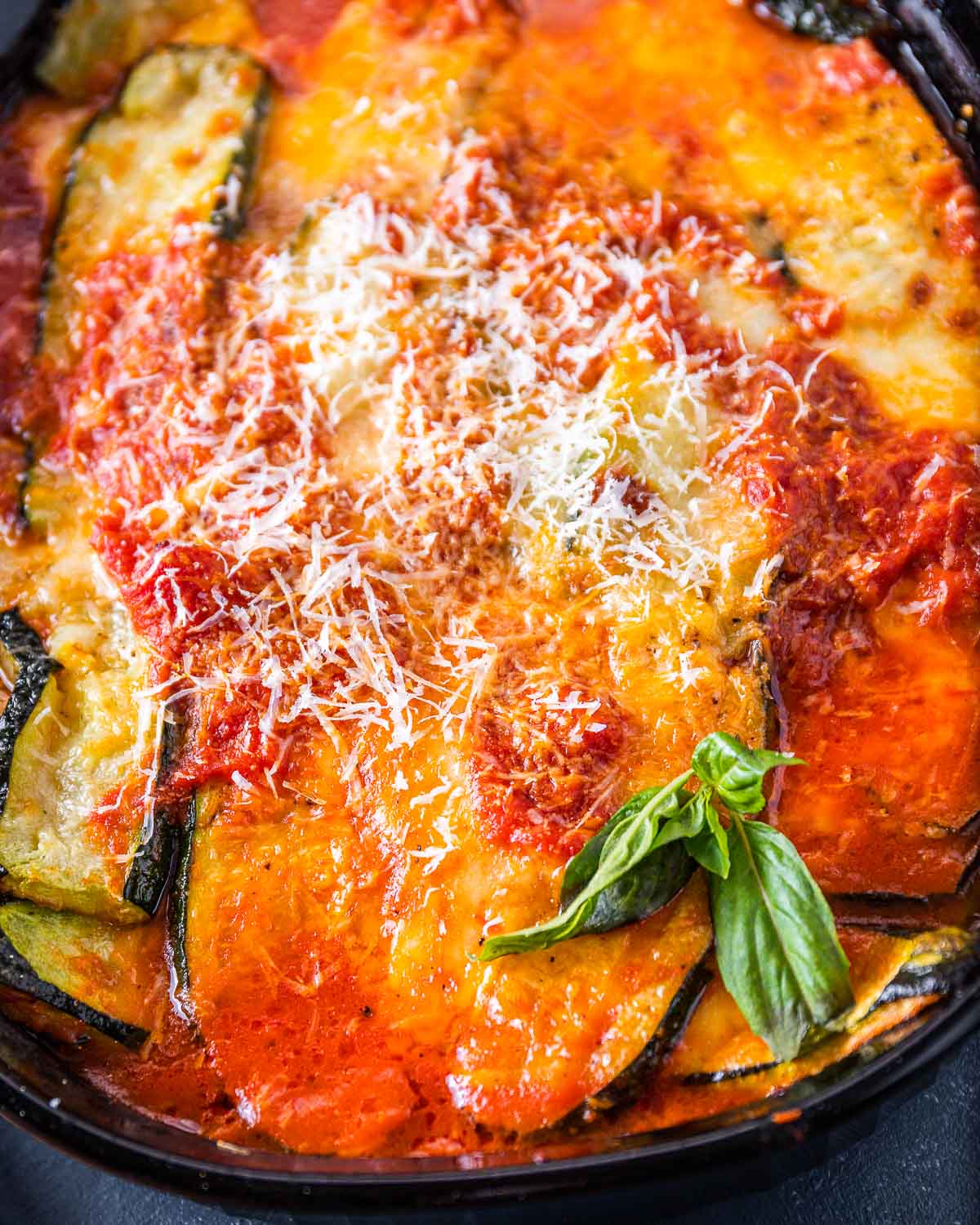 Black baking dish with cooked zucchini parm and basil garnish.