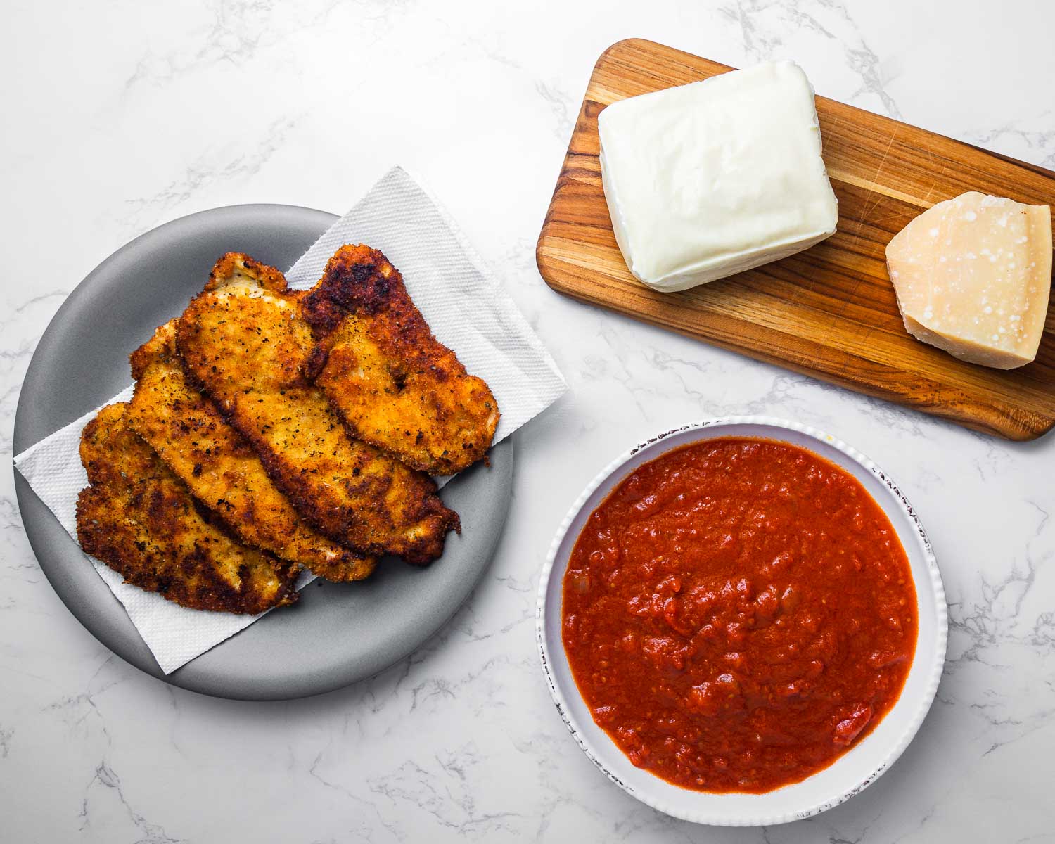 Ingredients shown: chicken cutlets, mozzarella cheese, parmesan cheese, and bowl of sauce.