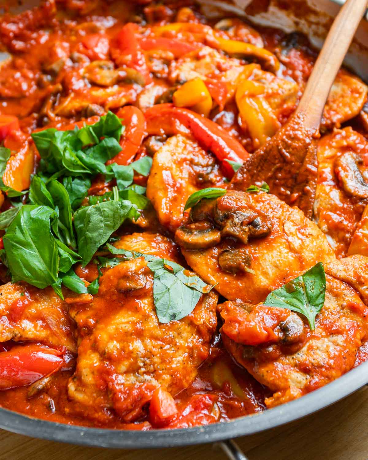 Large pan with chicken pizzaiola and wooden spoon.