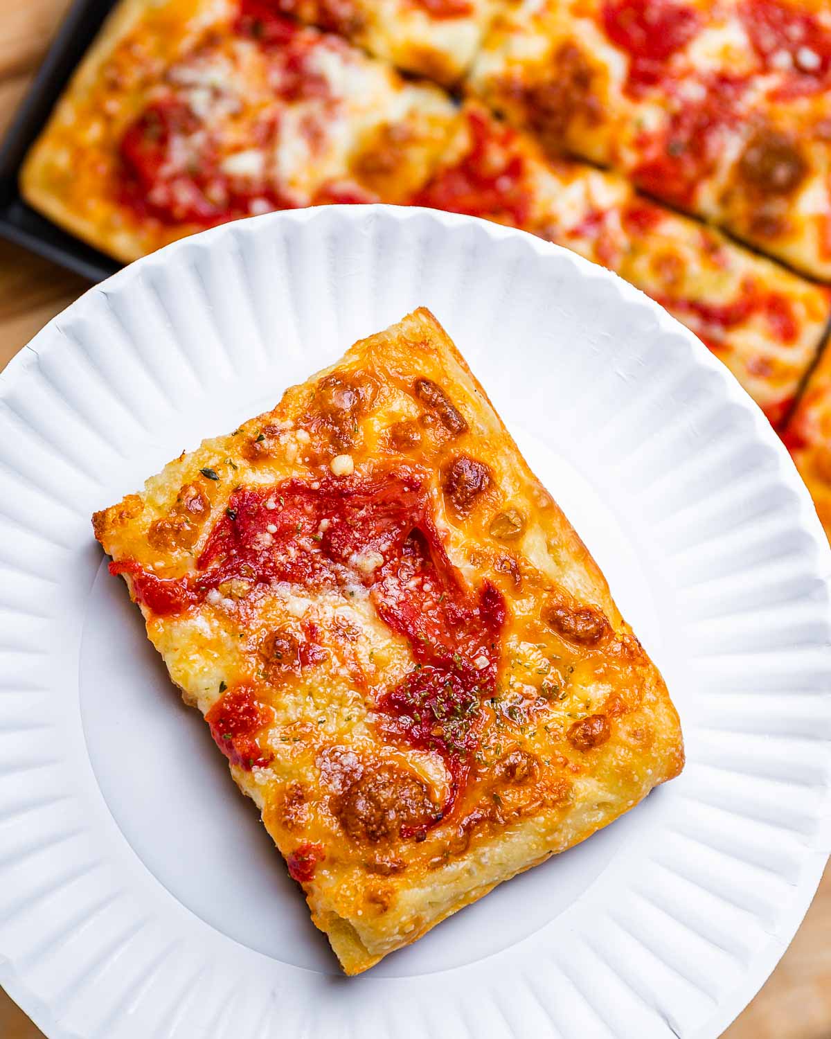 Slice of Grandma pizza in white plate with full pie below.