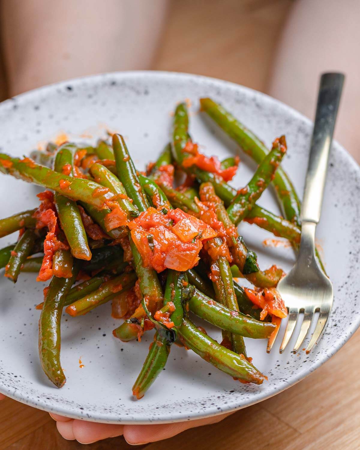 Green beans with tomato sauce on white plate held in hands.