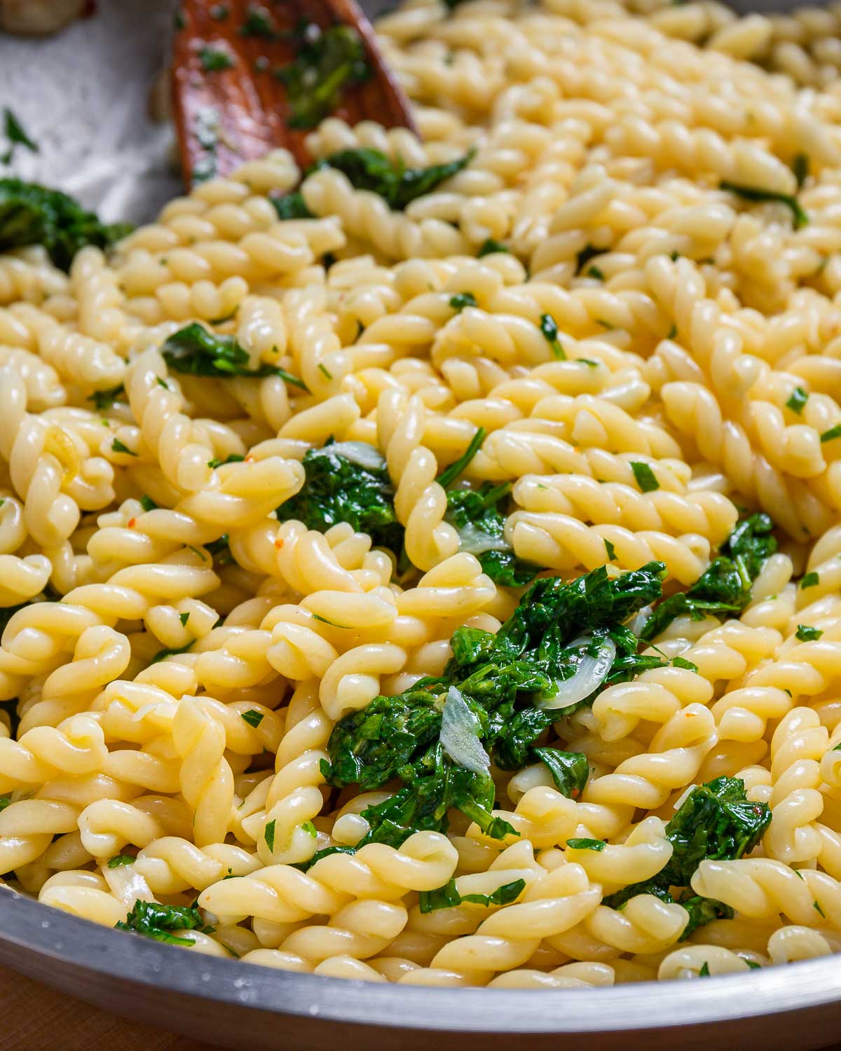 Large pan with pasta and arugula.