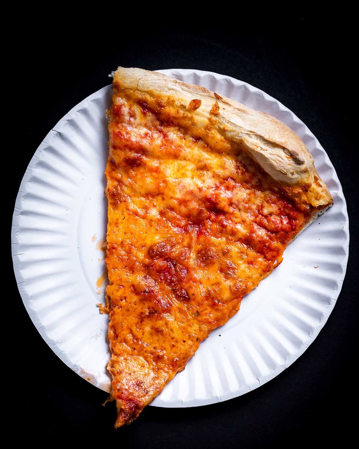 Slice of New York pizza in white plate.