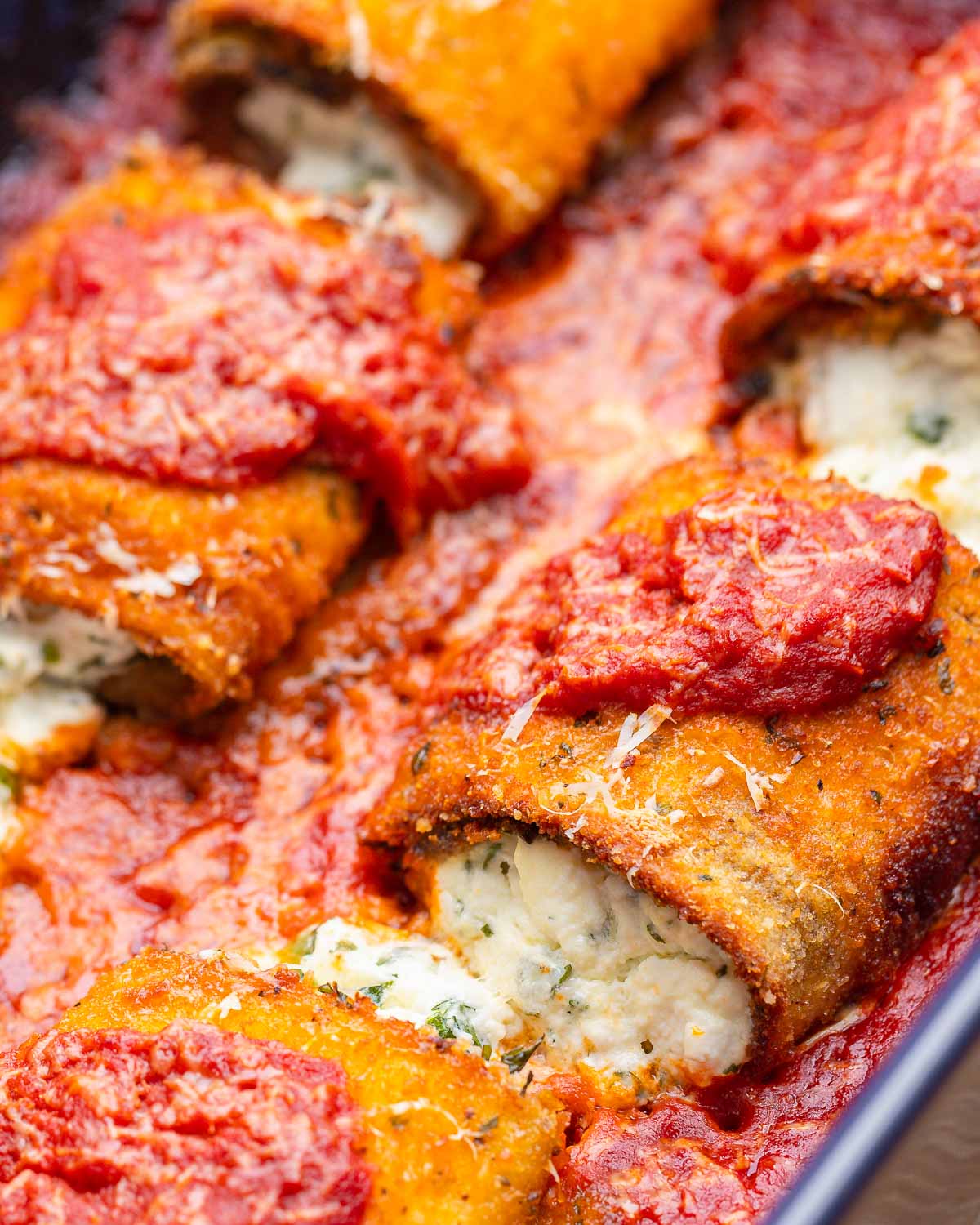Close up shot fried eggplant rollatini with ricotta cheese oozing out.