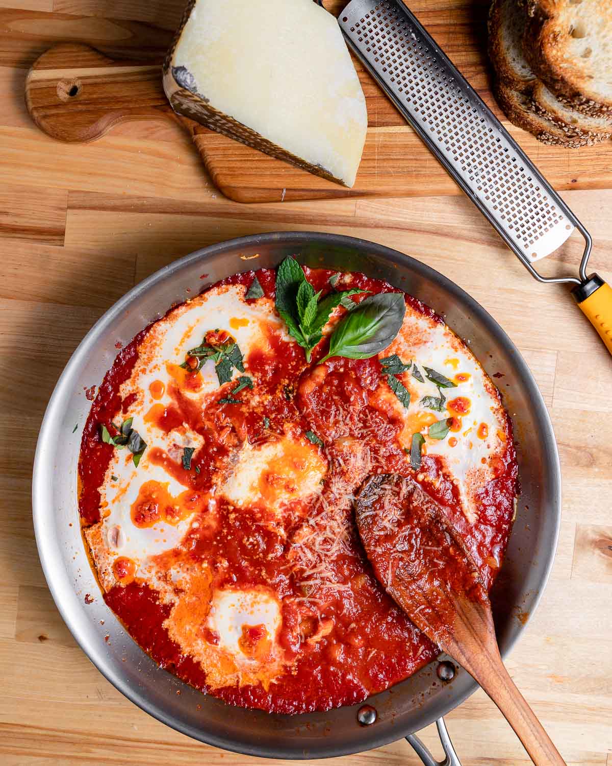 Pan of eggs in purgatory with cheese and bread on the side.