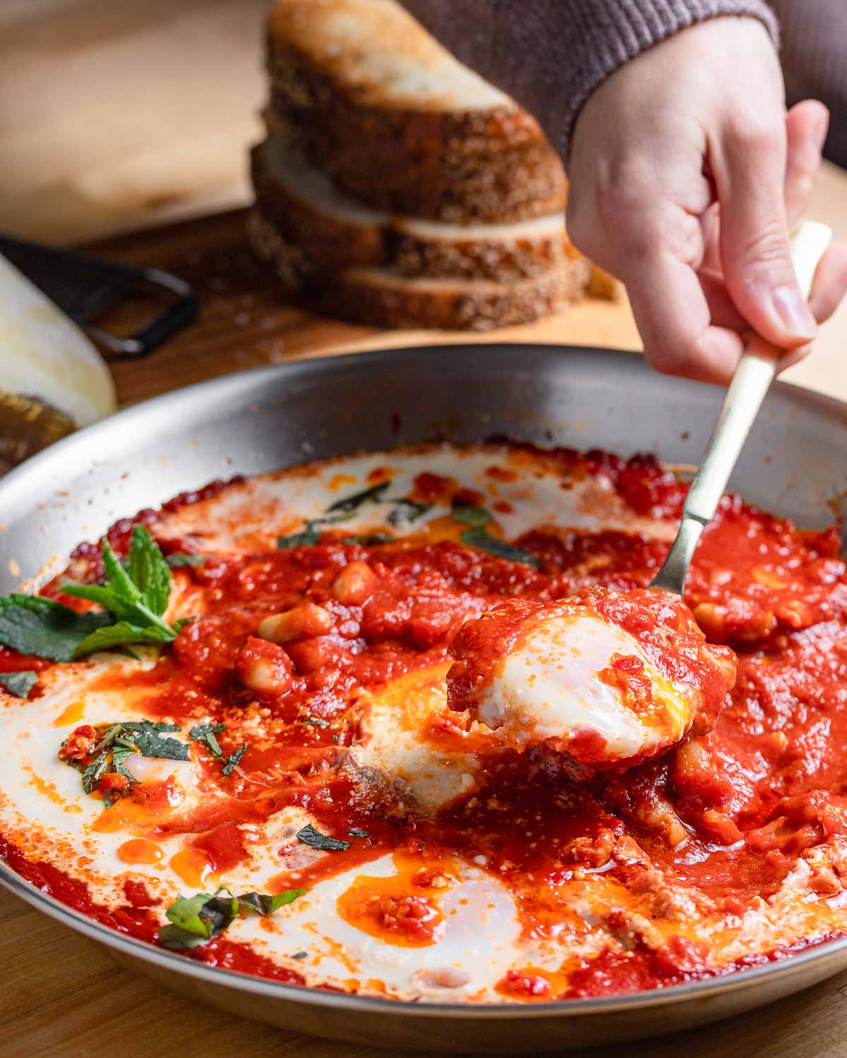 Spoon pulling out one poached egg from sauce pan.