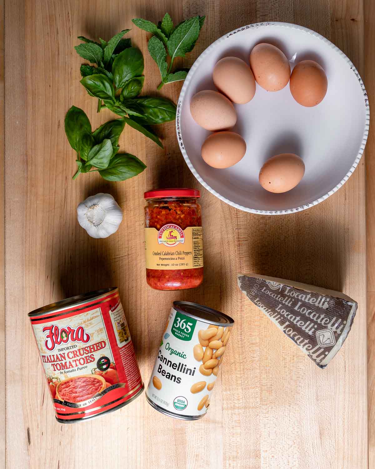 Ingredients shown: eggs, basil, mint, garlic, Calabrian chili paste, tomatoes, beans, and Romano cheese.