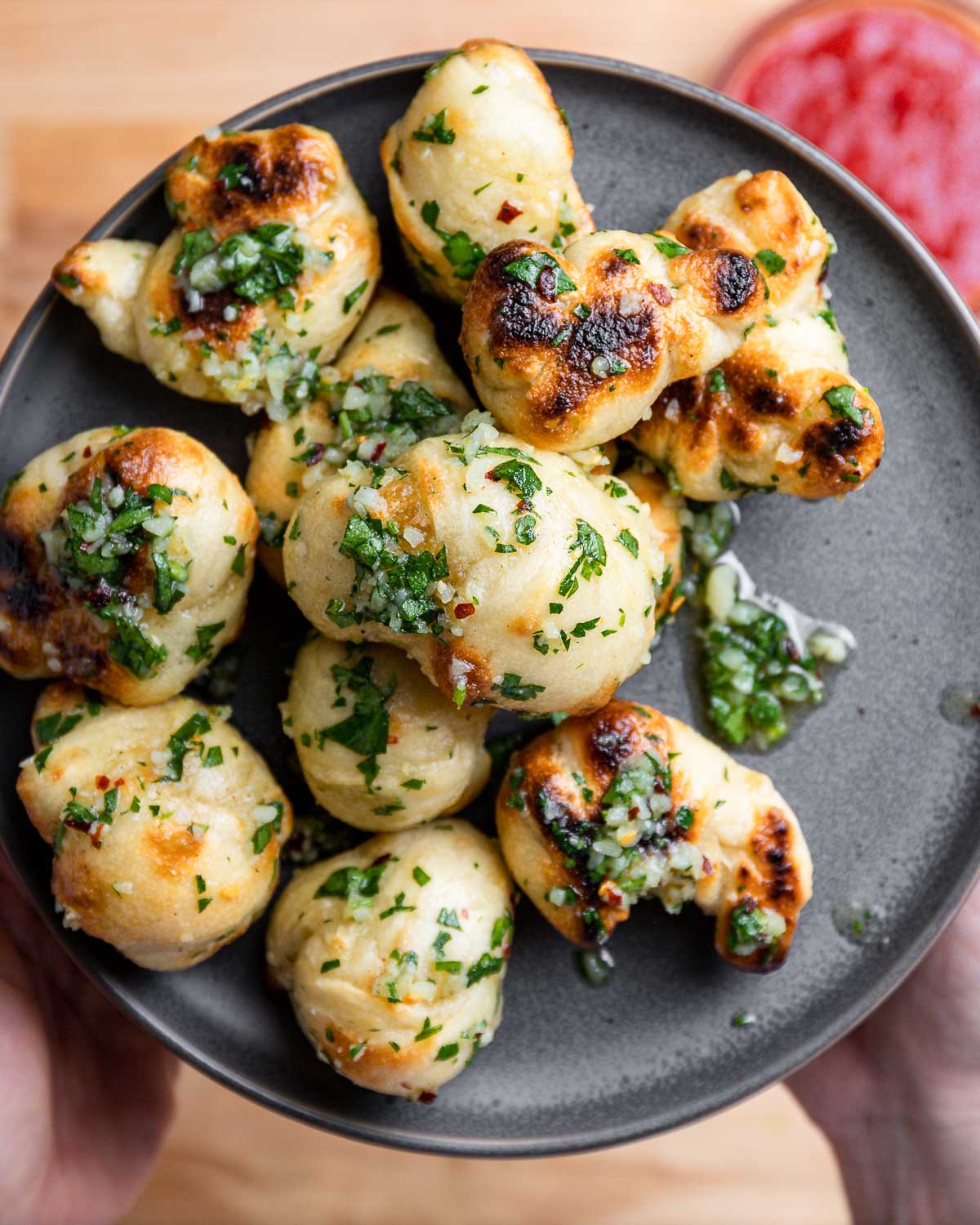 Hands holding garlic knots in grey plate.