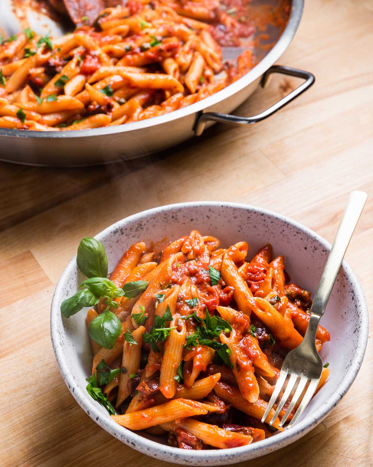 White bowl of penne puttanesca with fork.