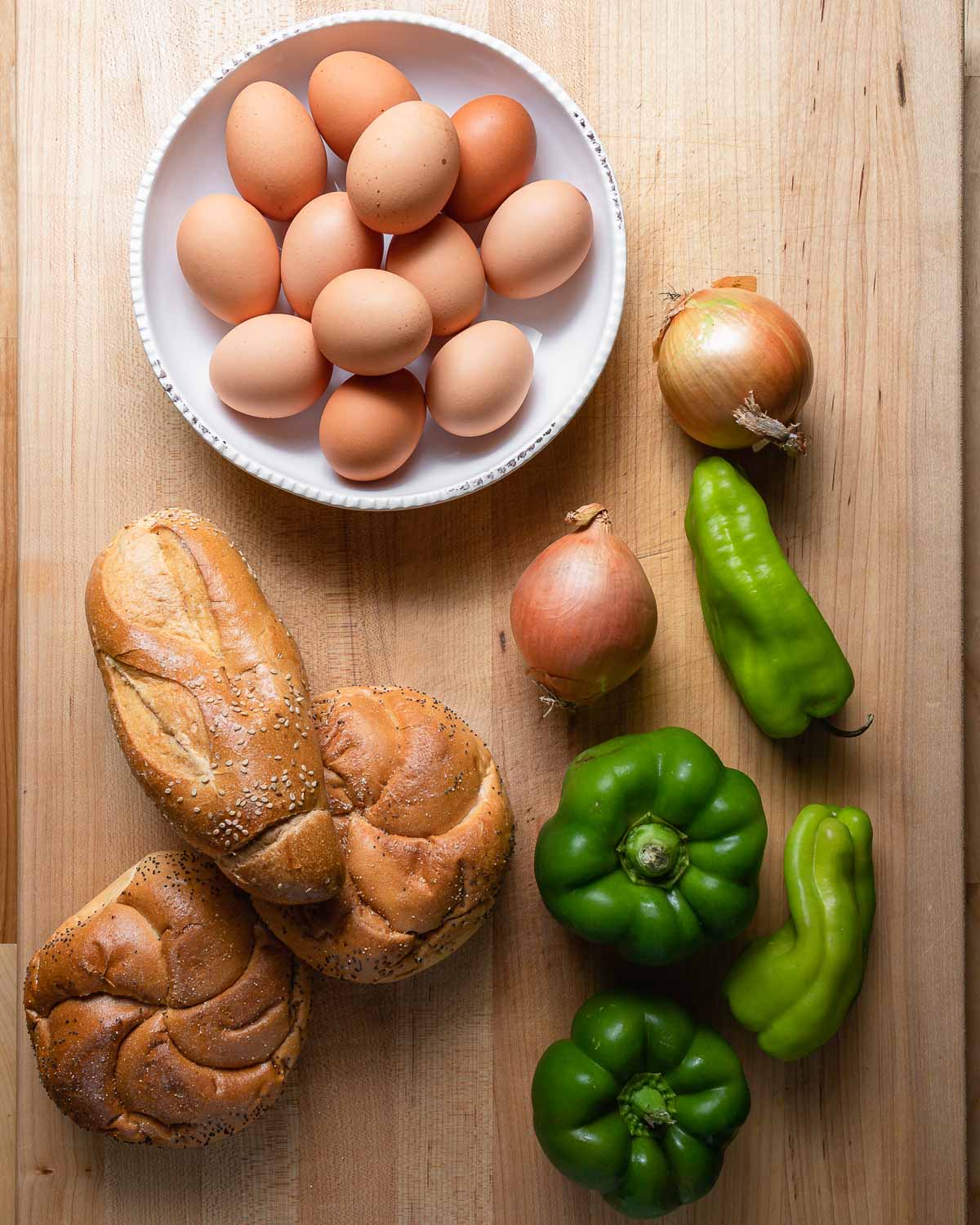 Ingredients shown: bowl of eggs, onions, peppers, hero and round rolls.