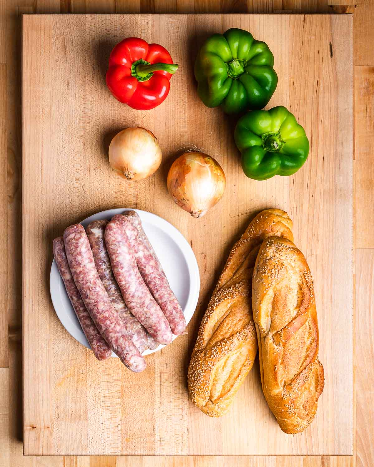 Ingredients shown: red and green bell peppers, onions, Italian sausage links, and Italian bread.