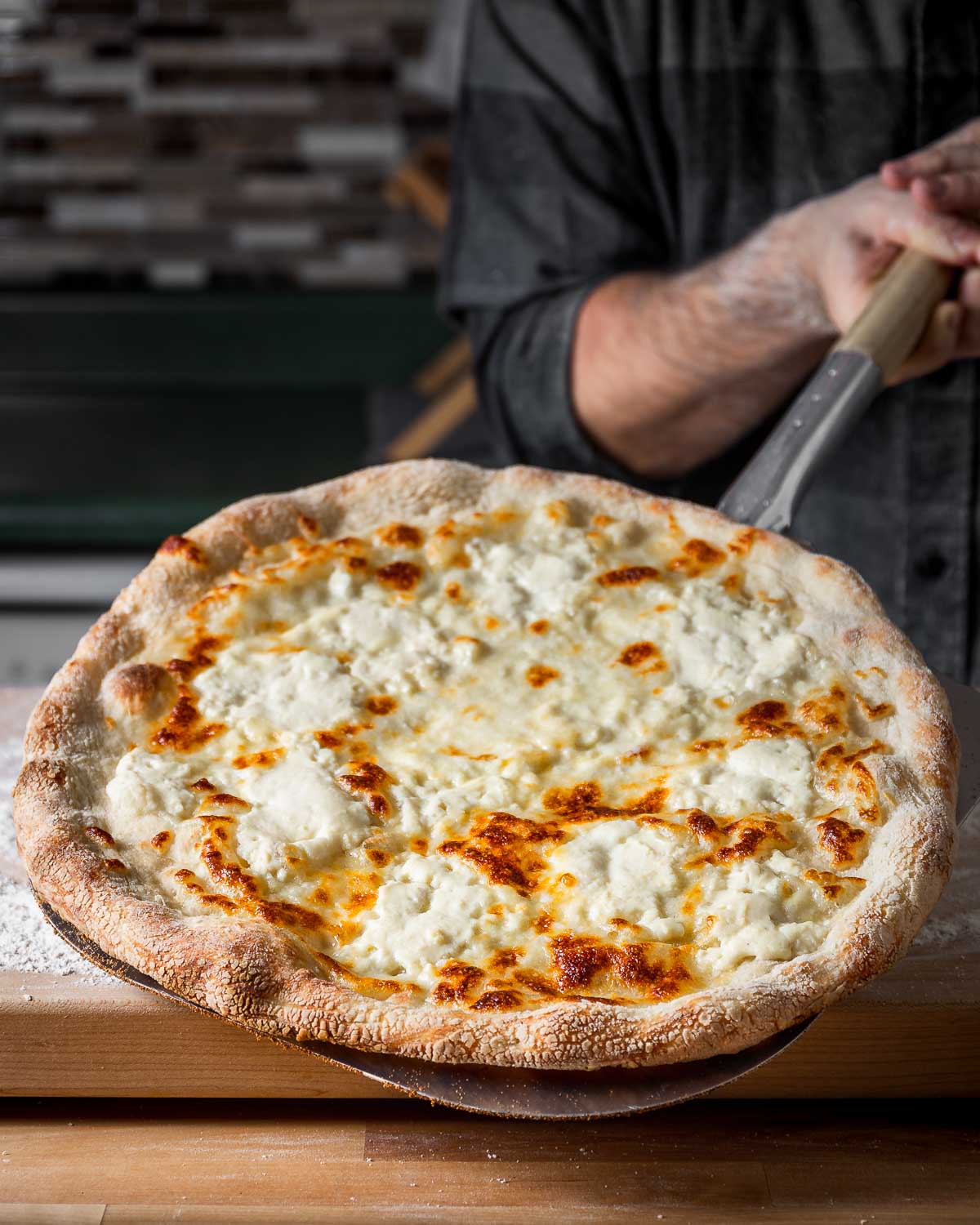 Full white pizza held by metal pizza peel.