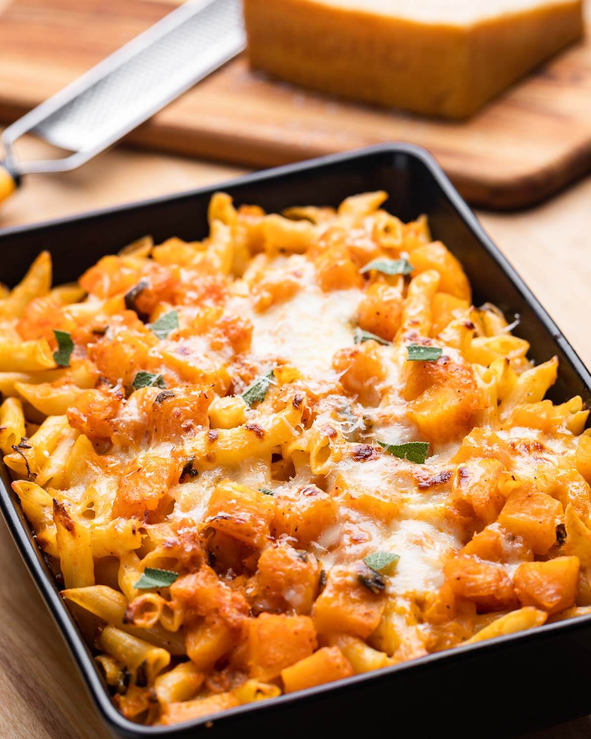 Baking dish with baked butternut squash pasta and block of Parmigiano Reggiano in background.