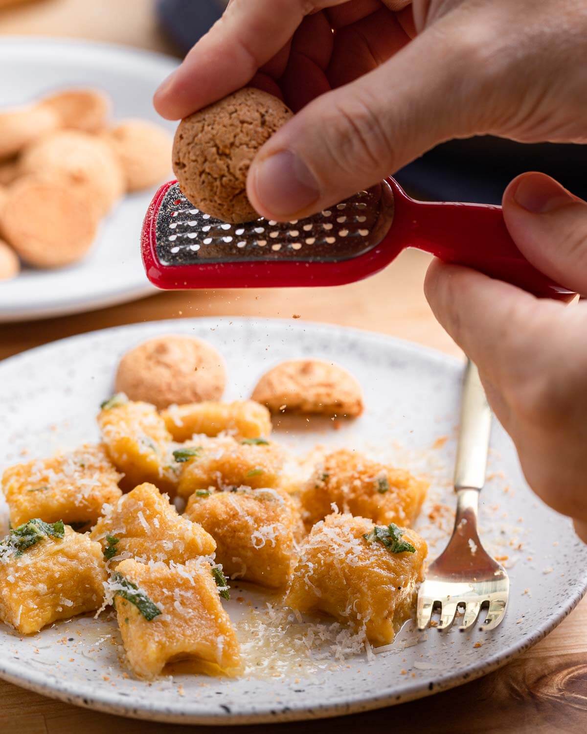 Grating amaretti cookie on top of plate of butternut squash gnocchi.