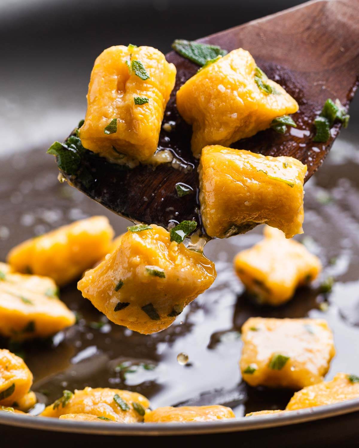 Walnut spoon tossing butternut squash gnocchi in pan.