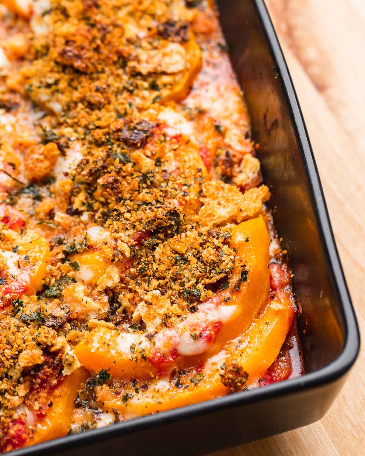 Butternut squash parmigiana in black baking dish.