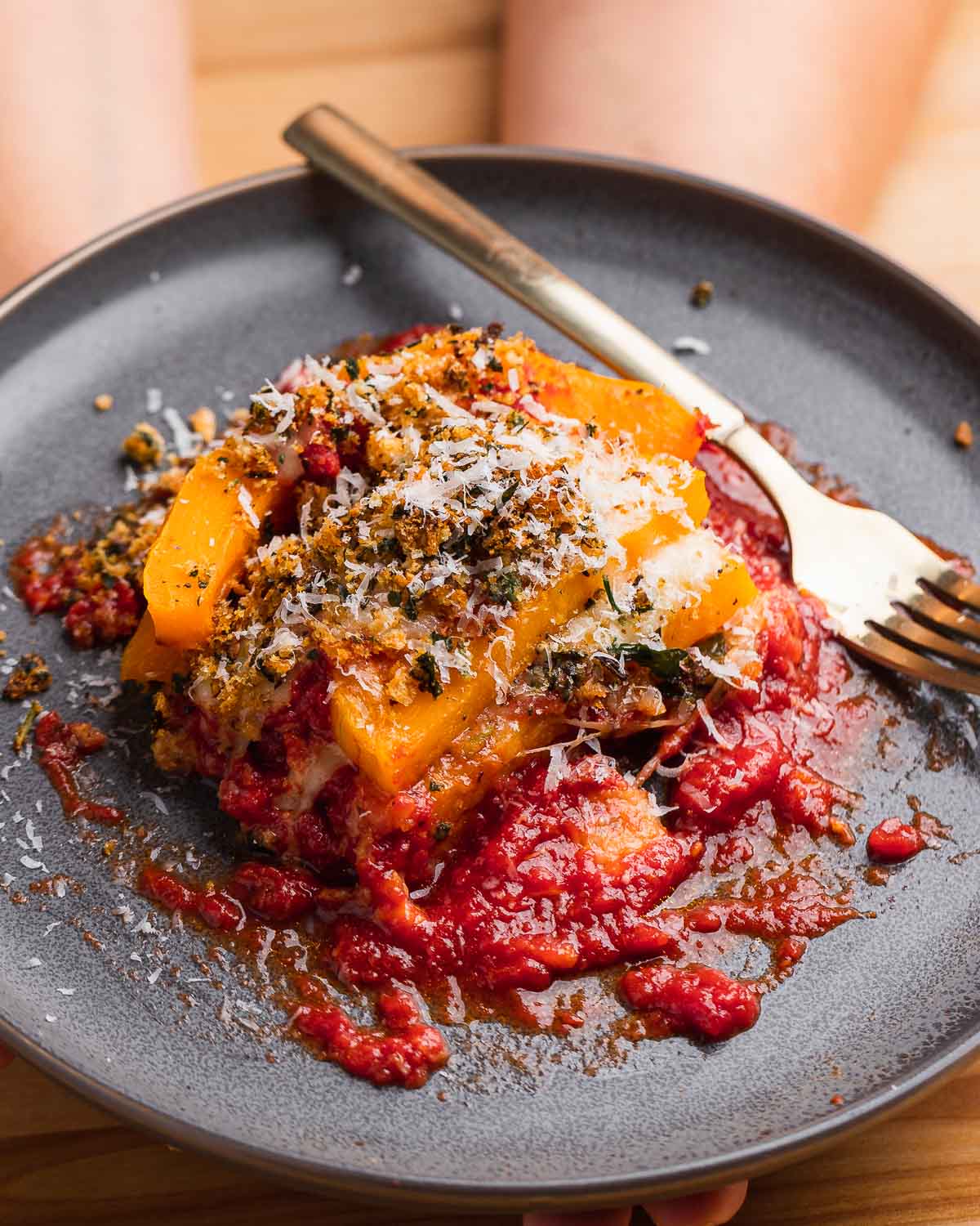 Hands holding plate of butternut squash parm.