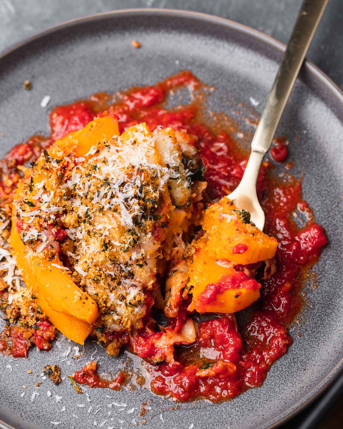 Butternut squash parmigiana in grey plate with fork holding piece.