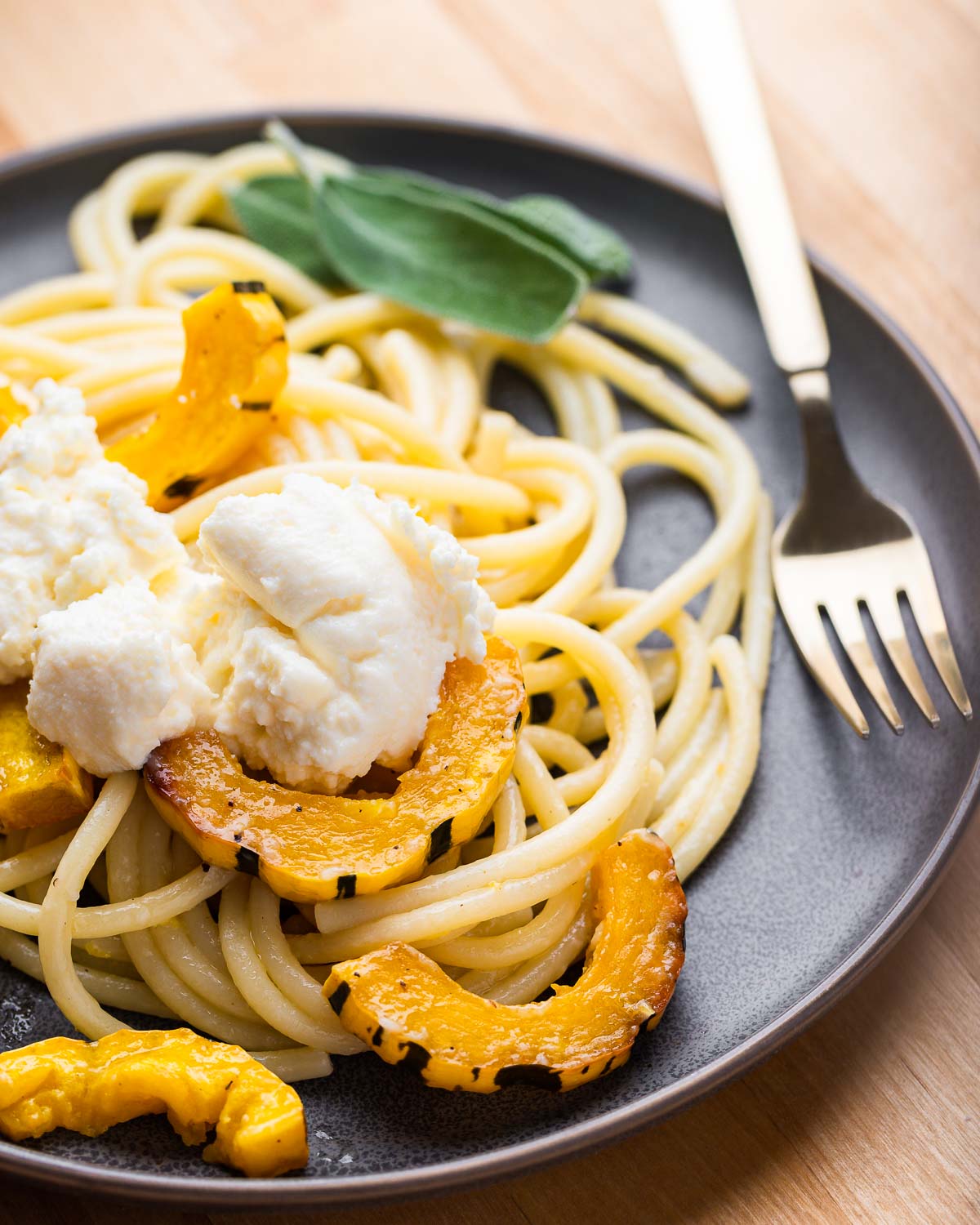 Grey plate with delicata squash bucatini and dollop of ricotta on top.