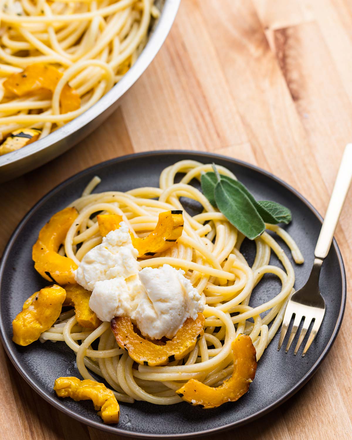 Grey plate with delicata squash pasta and dollop of ricotta on top.