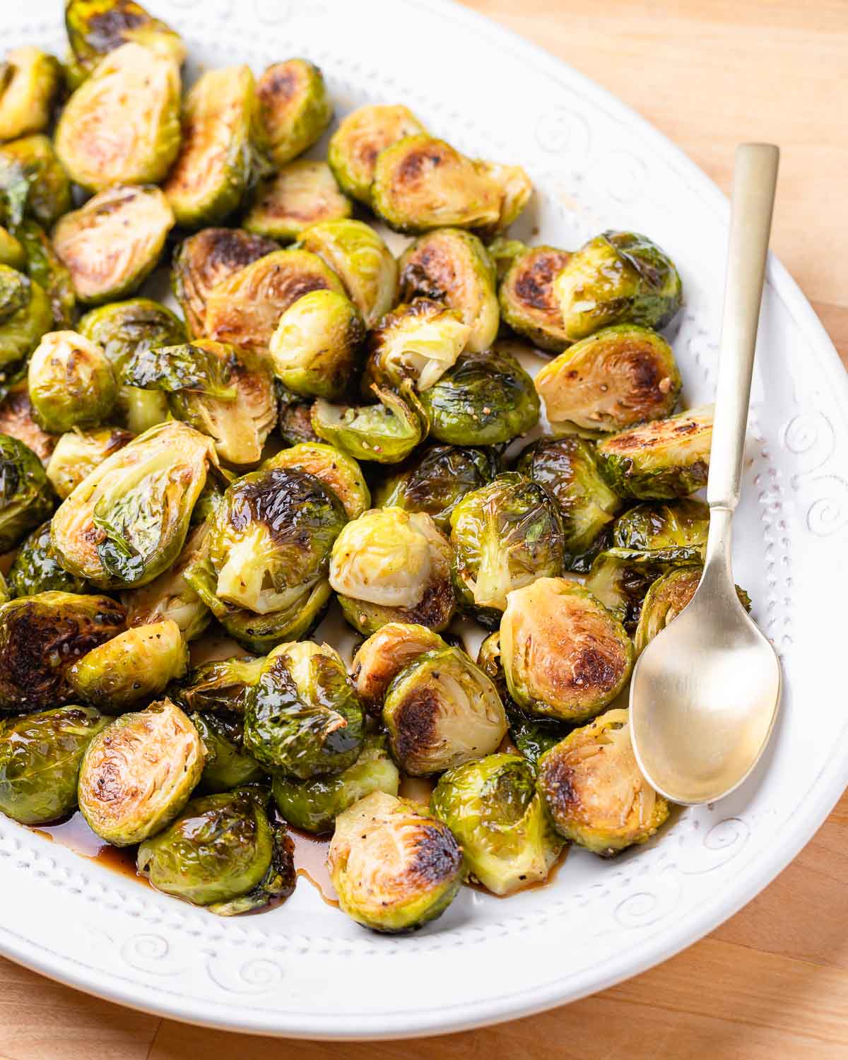 Plate of honey balsamic brussels sprouts in white plate with gold spoon.