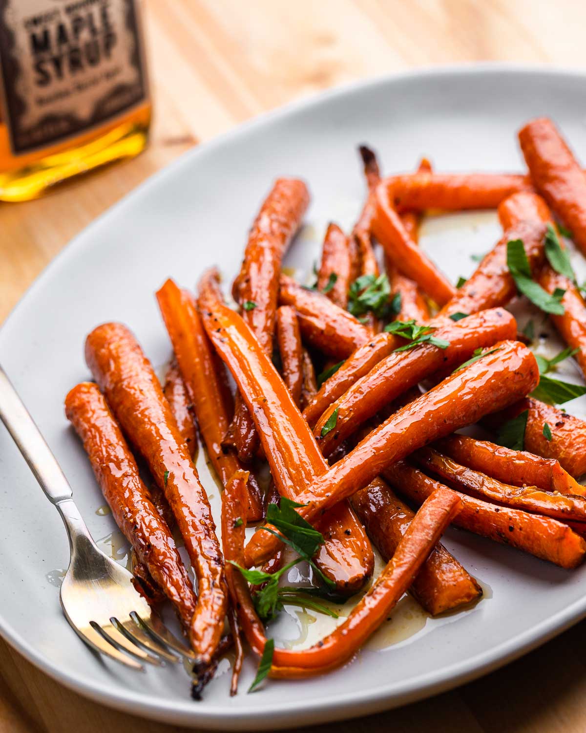 Large plate with maple roasted carrots and bottle of maple syrup.