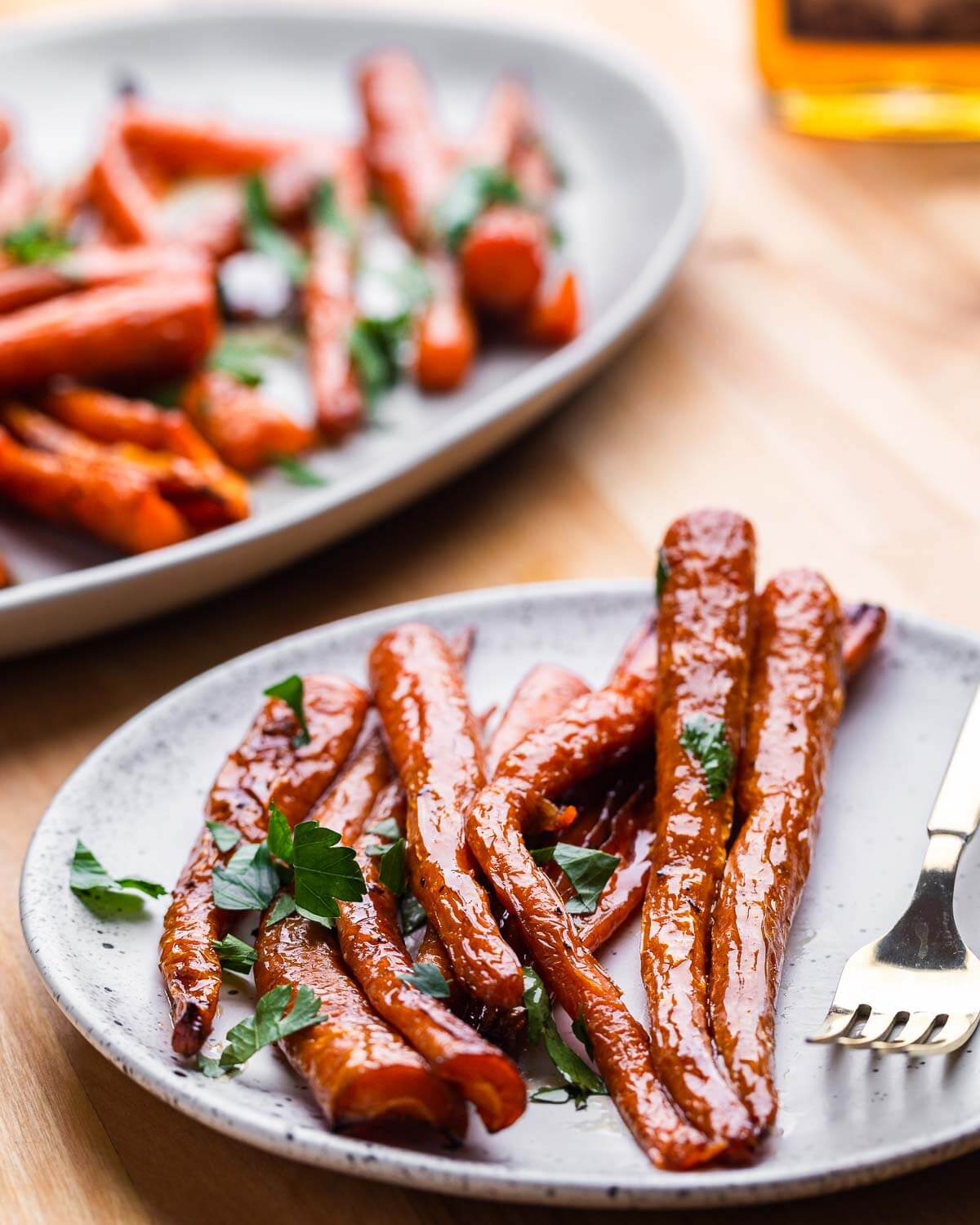 White plate with glazed carrots and large plate in background.