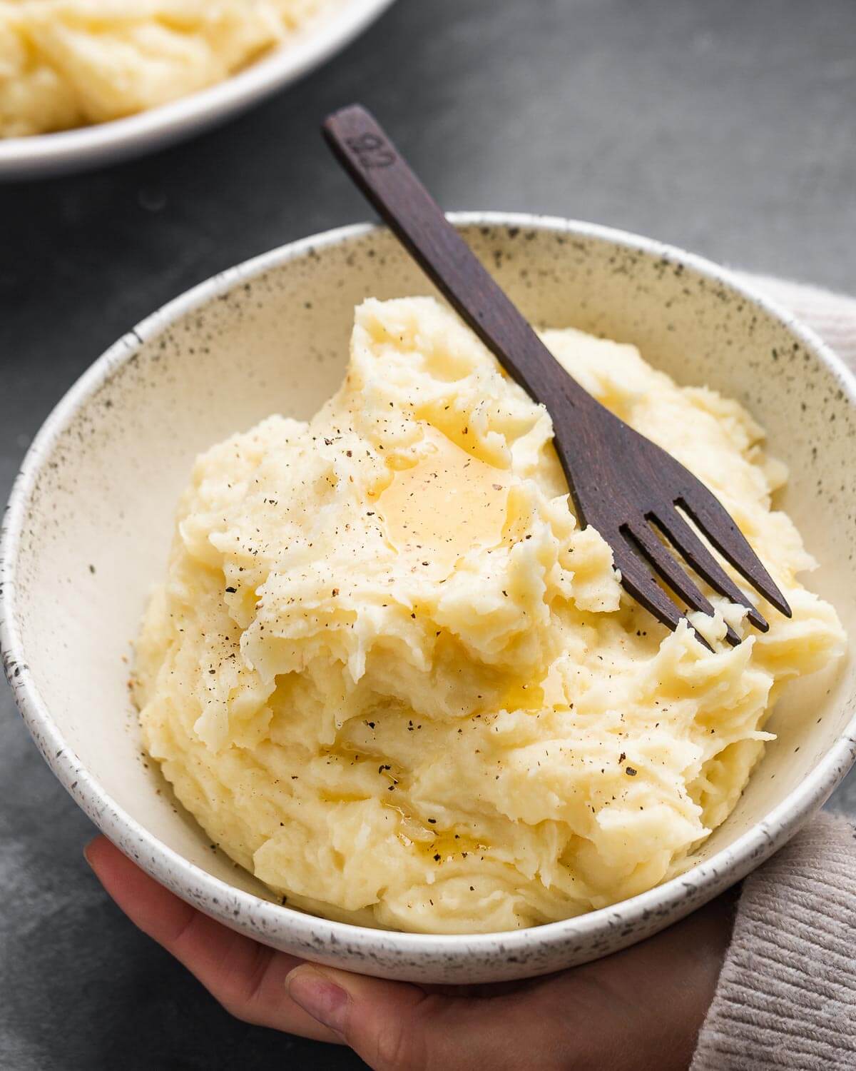 Hands holding white bowl of roasted garlic mashed potatoes.