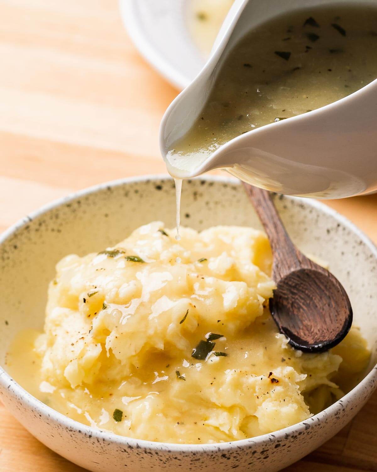 Gravy poured onto white bowl with mashed potatoes.