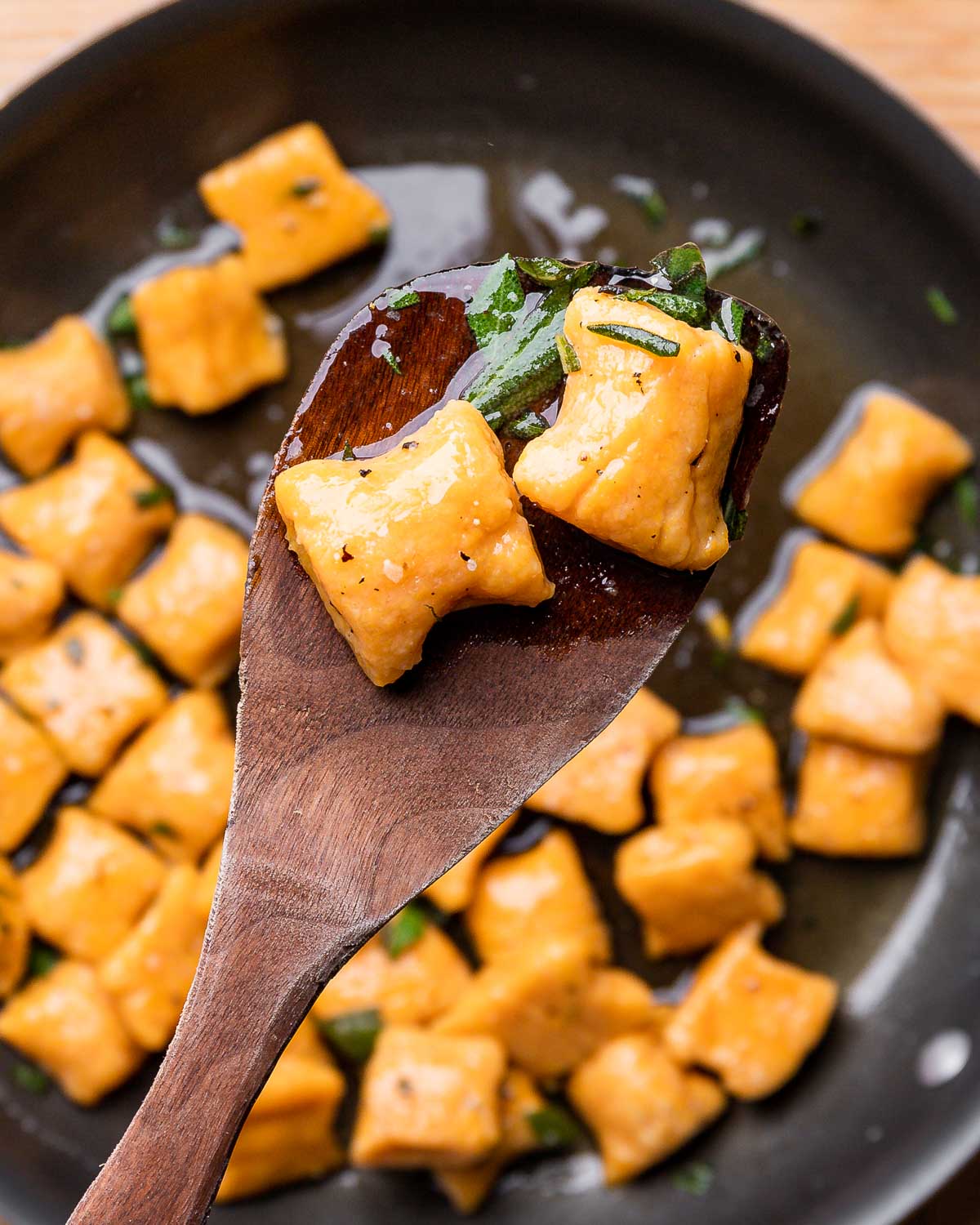 Wooden spoon holding 2 cooked sweet potato gnocchi.