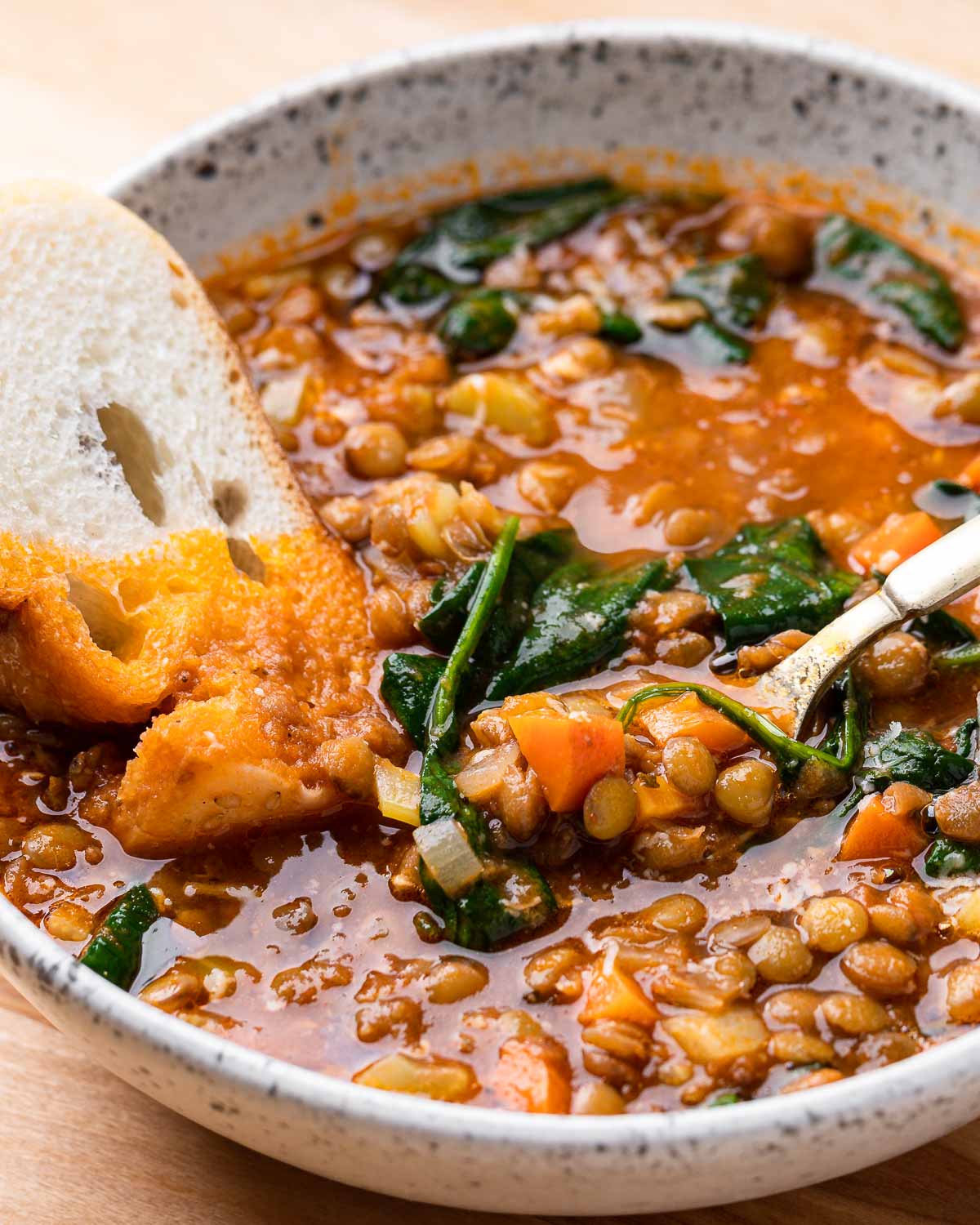 White bowl with Italian lentil soup and piece of bread.