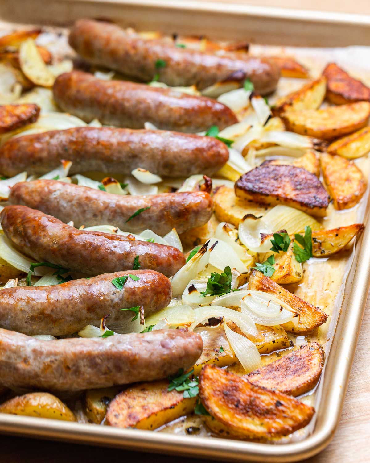 Gold pan with cooked roasted potatoes and Italian sausage.