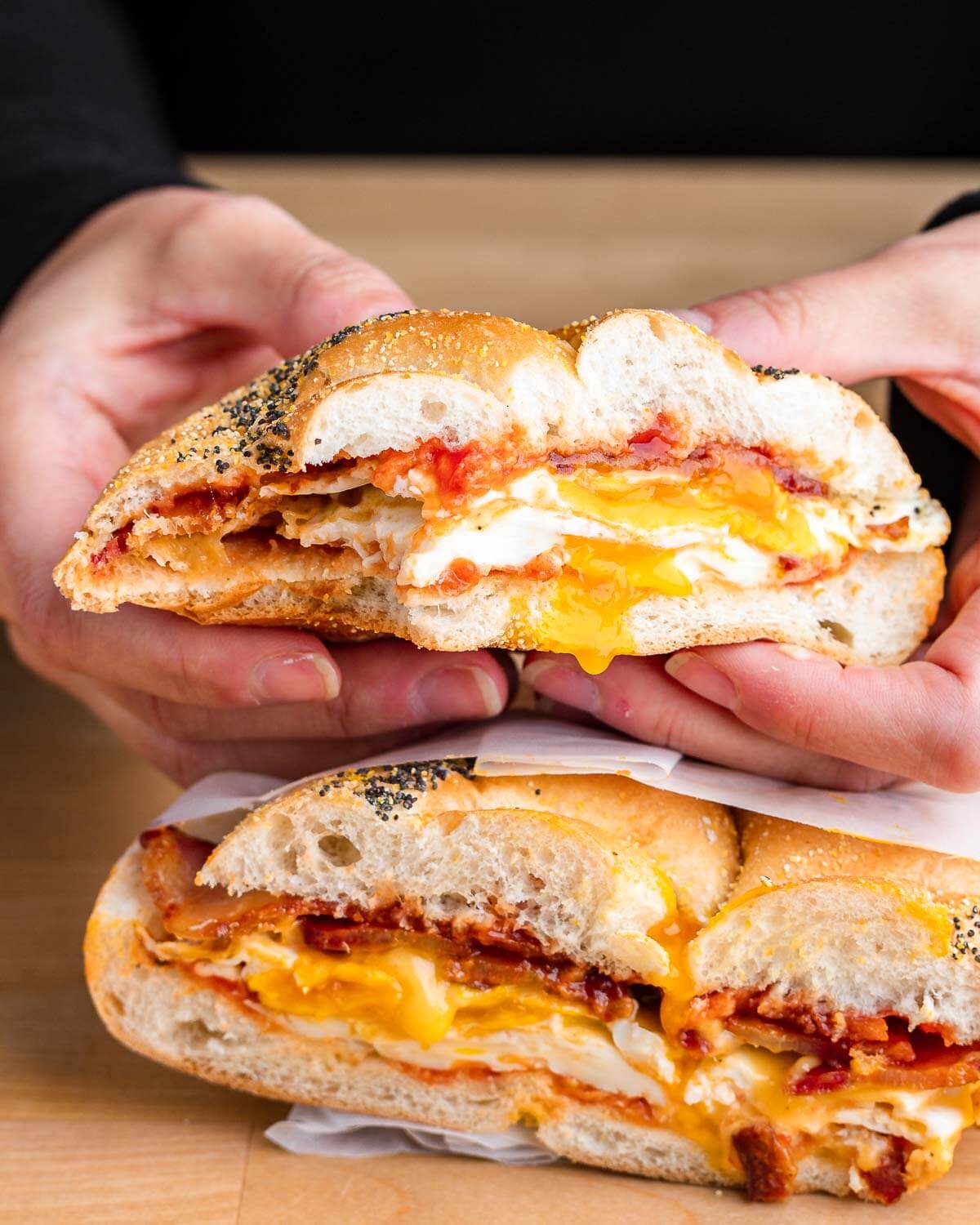 Hands holding half a bitten bacon egg and cheese sandwich.