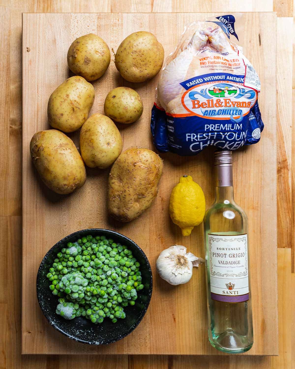 Ingredients shown: potatoes, whole chicken, peas, lemon, garlic, and white wine.