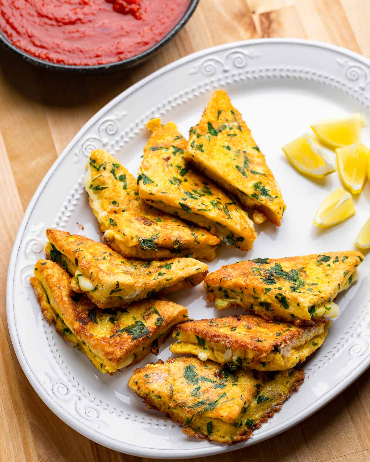 Mozzarella en carrozza triangles in white plate with lemon wedges.