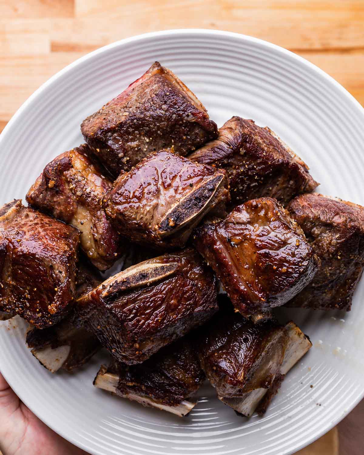 Seared short ribs held in white plate.